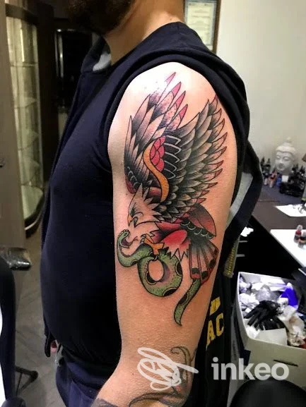 Tatuaggio a colori di aquila che afferra un serpente sull'omero, realizzato da INK-IOSTRO a Zagarolo.