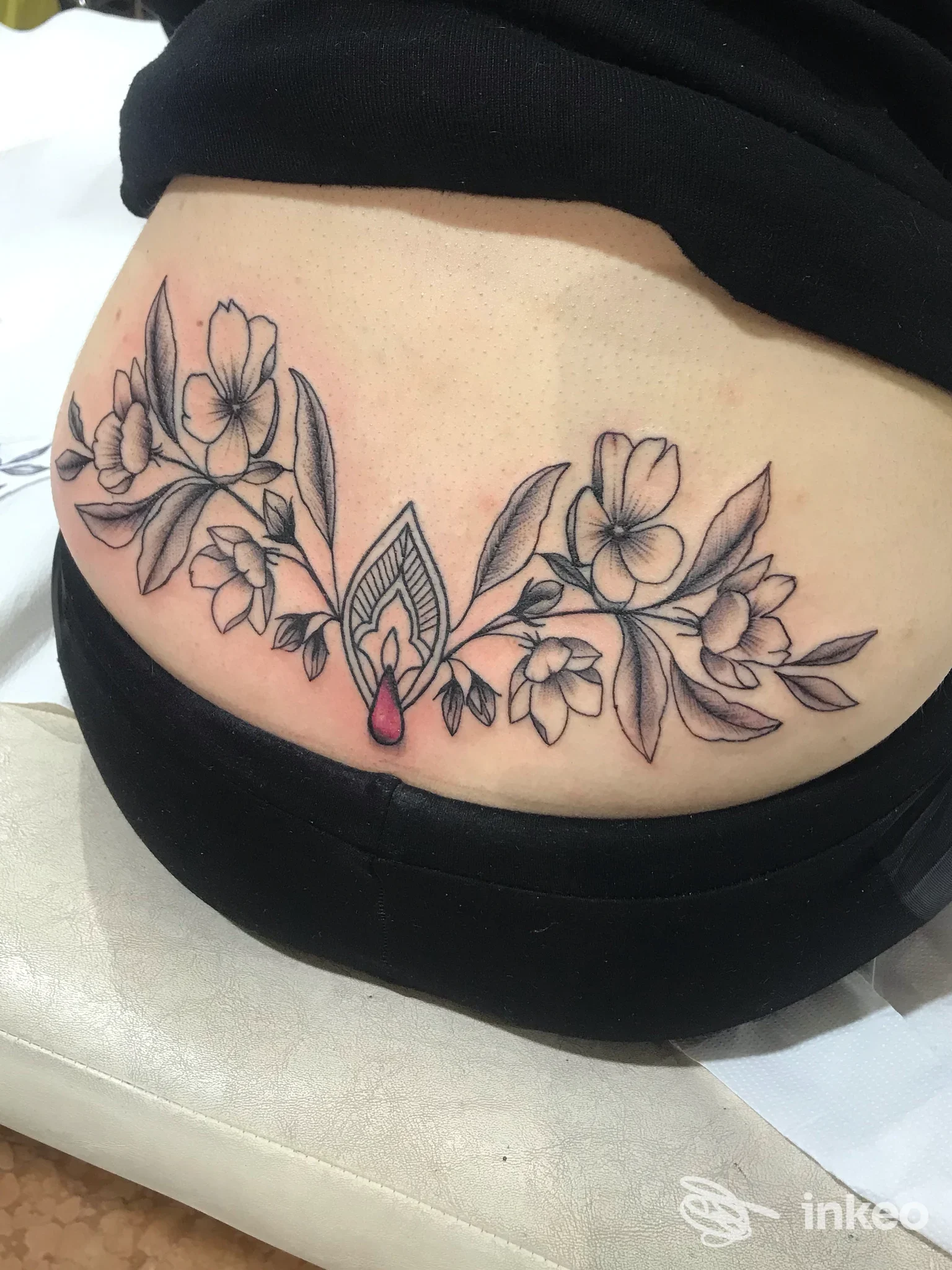 Tatuaggio floreale in bianco e nero con piccolo dettaglio rosso sul fianco/bassa schiena, fotografato per INK-IOSTRO Zagarolo.