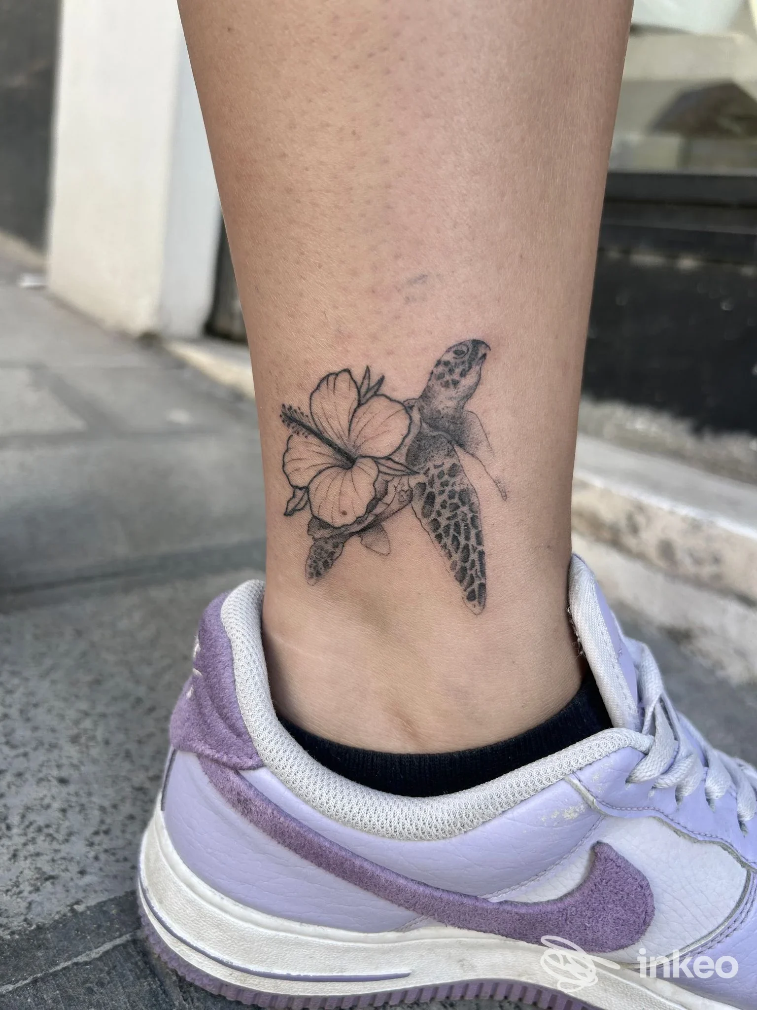 Tatuaggio di tartaruga con fiore sulla caviglia, realizzato da Industrial Ink a Frosinone, dettaglio in nero e grigio.