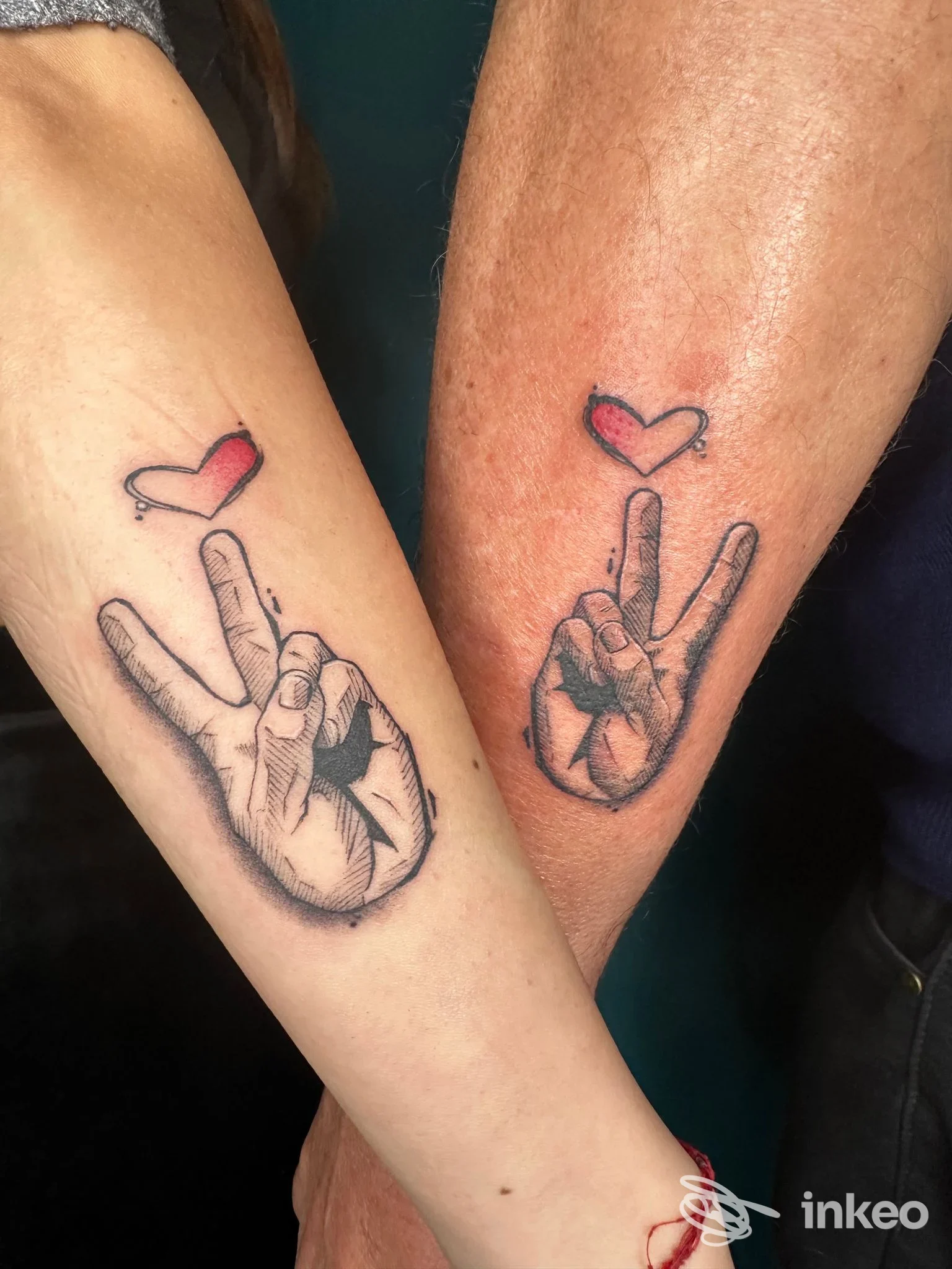 Due avambracci con tatuaggi abbinati: mano che fa il segno di pace e piccolo cuore rosso, foto dallo studio Jelly Parson a Genzano di Roma.