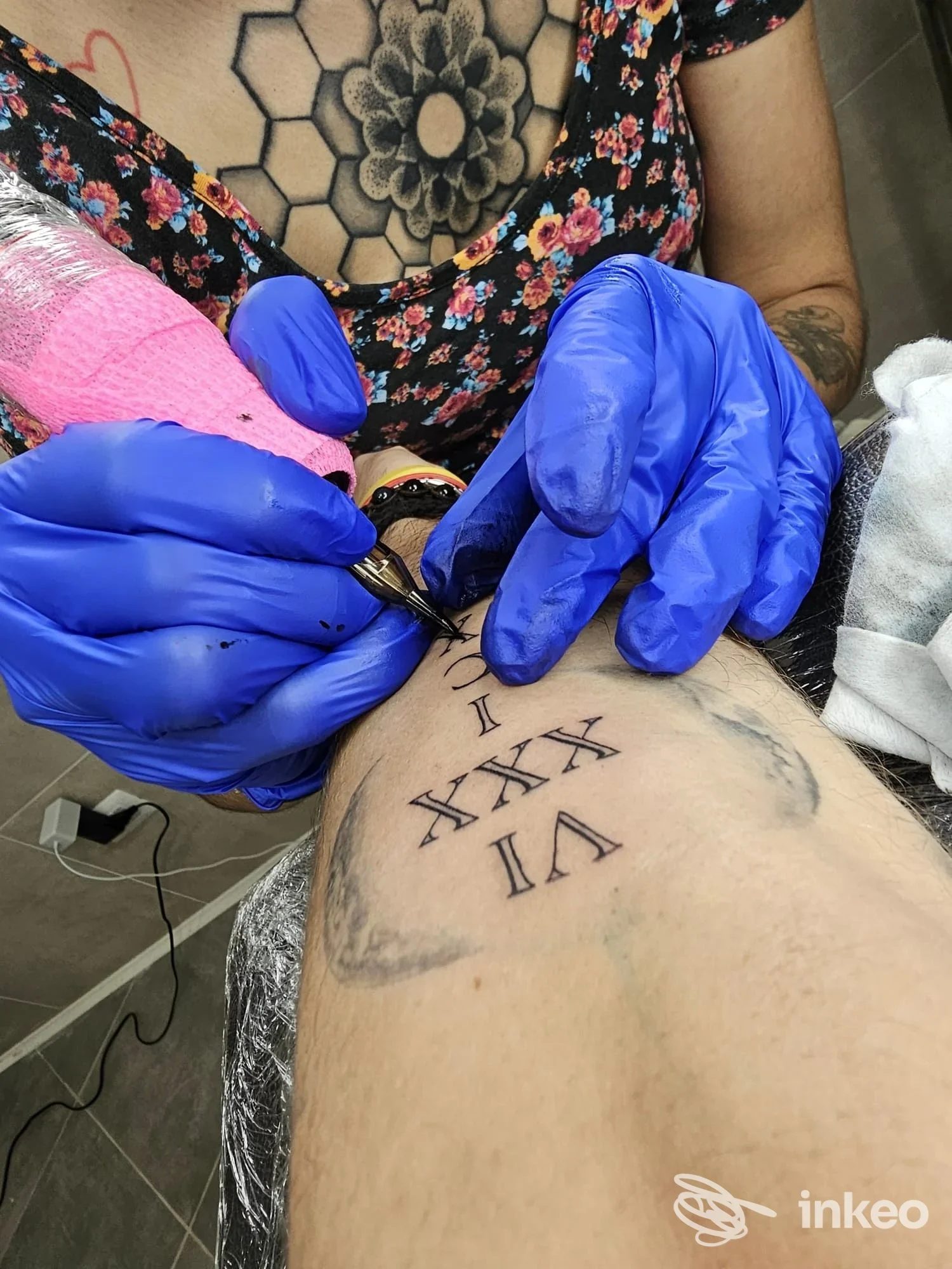 Tatuaggio di numeri romani sul bicipite eseguito da Guna Tattoo Lab a Santi Cosma e Damiano, vista ravvicinata dell'operatrice al lavoro.
