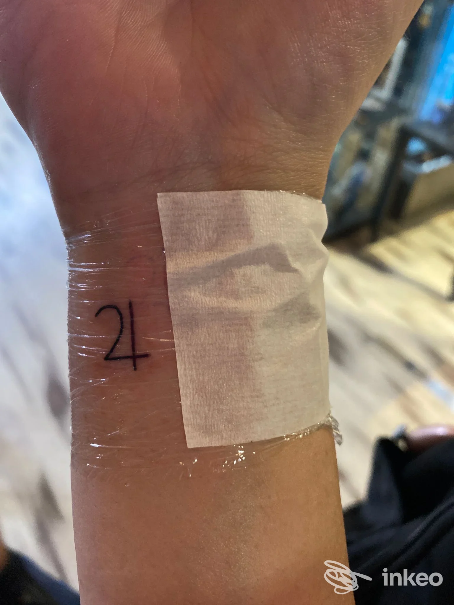 Primo piano di un piccolo tatuaggio lineare sul polso, coperto da pellicola e garza dopo il trattamento; Imperium Artis - Tattoo e piercing Studio Colosseo, Roma.