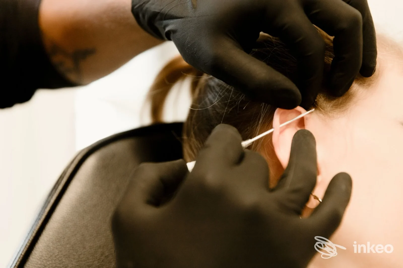 Primo piano di un'operazione di piercing sull'orecchio, con mani guantate che tengono l'orecchio e uno strumento vicino al lobo in studio.