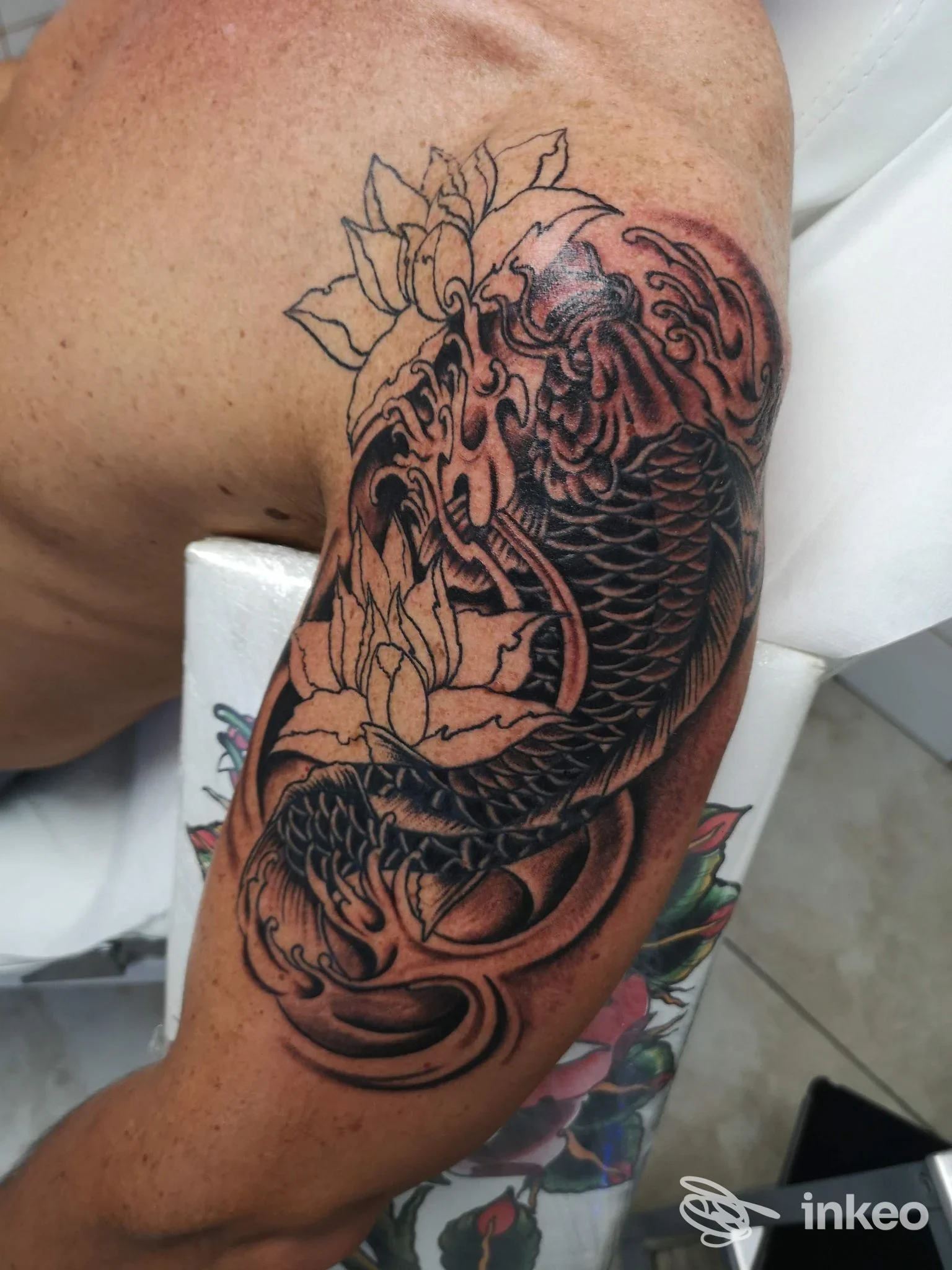 Fotografia del braccio superiore con grande tatuaggio di carpa koi e fiori in nero/grigio, realizzato nello studio ROMA INK a Roma.