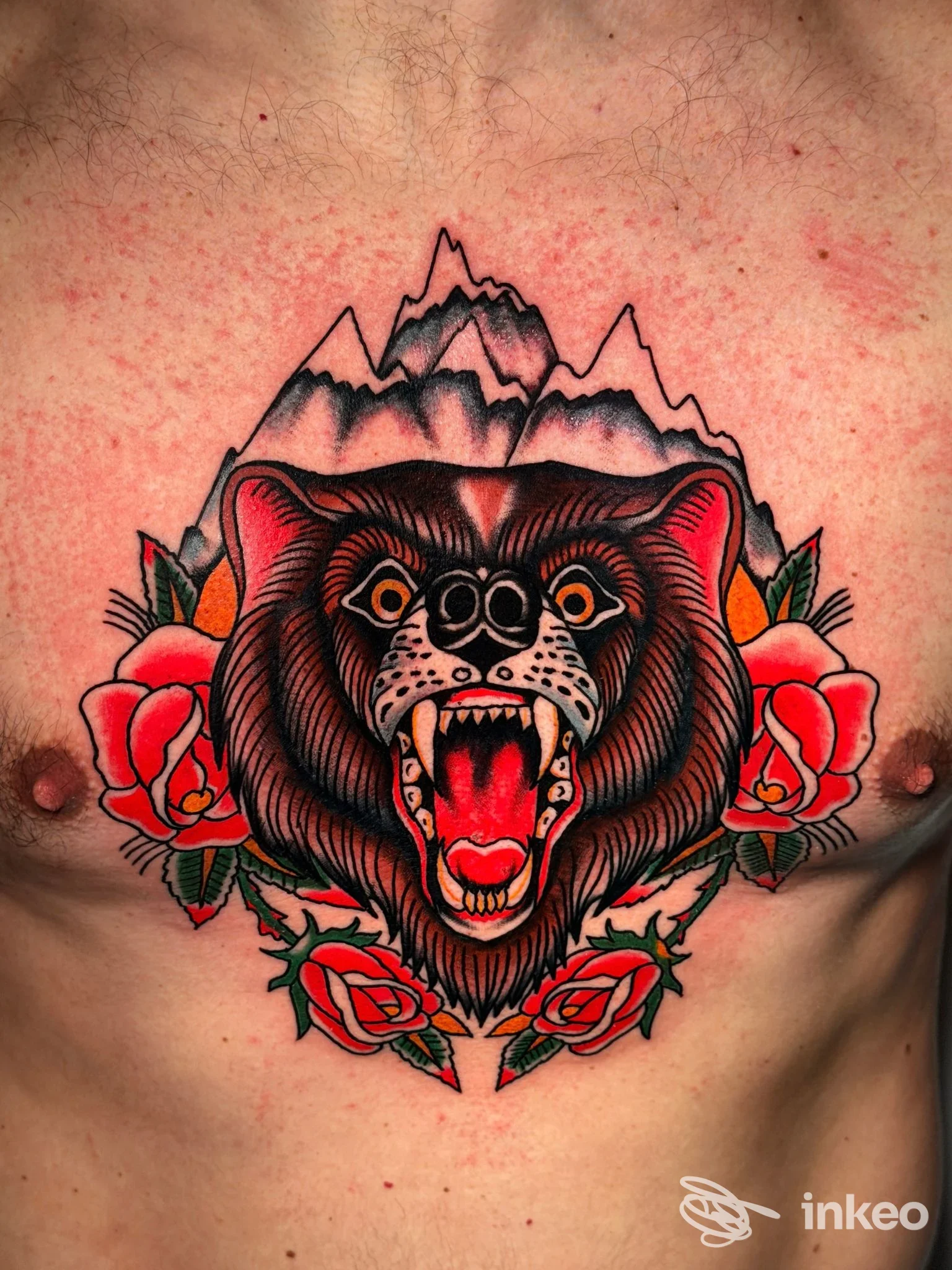 Grande tatuaggio tradizionale di orso ruggente con rose e montagne sul petto, realizzato da Square Mentality Marconi a Roma.