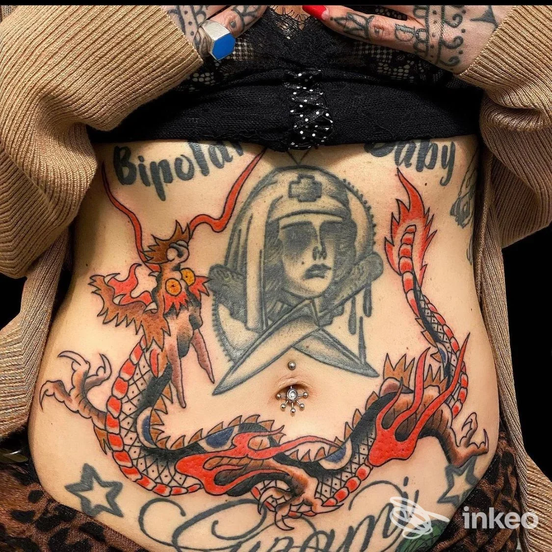 Primo piano dell'addome tatuato con drago e ritratto, con piercing all'ombelico. Tattooing Demon Studio, Roma.