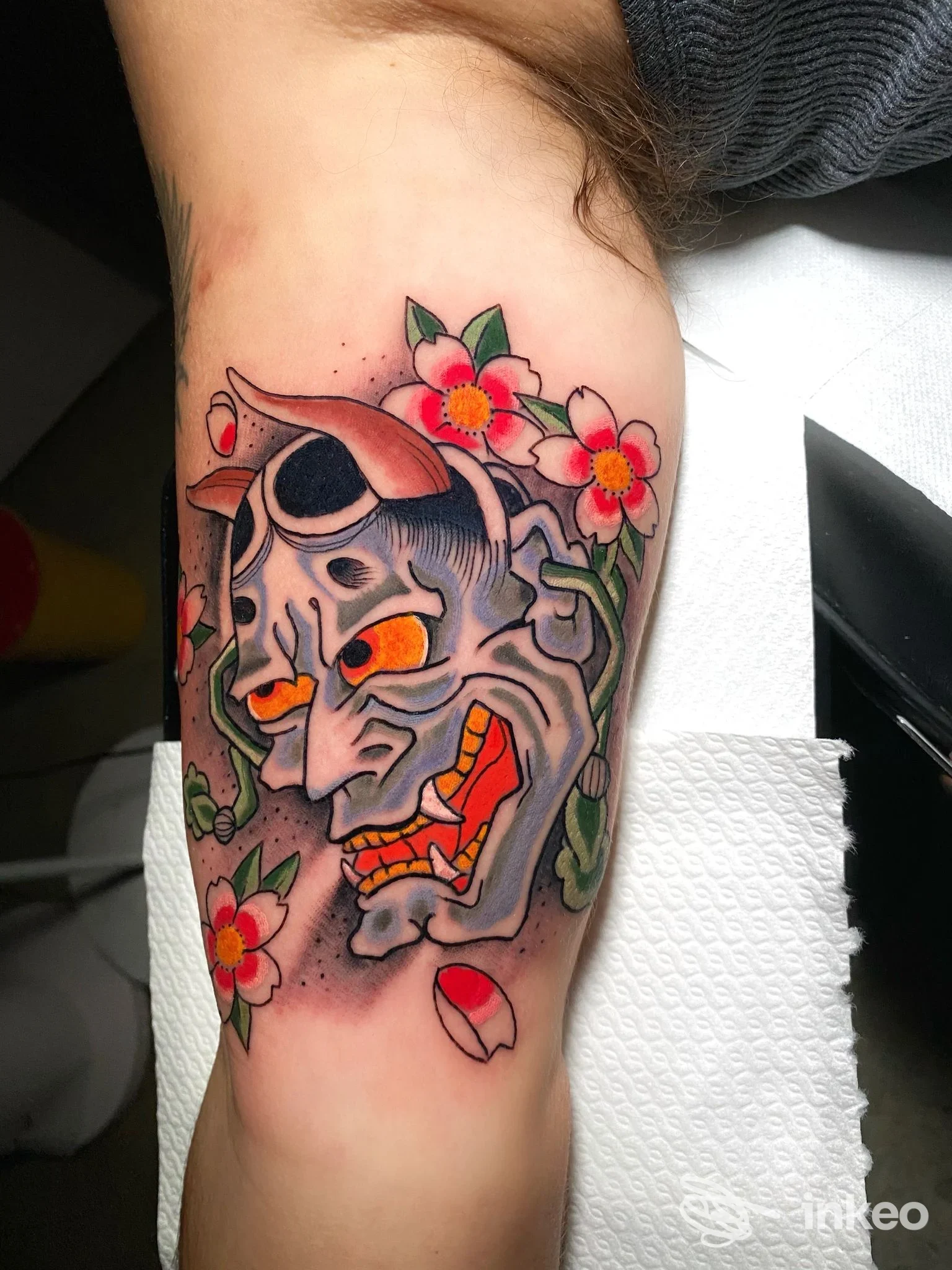 Tatuaggio maschera demone con fiori sull'interno braccio, realizzato da Tattooing Demon Studio a Roma.