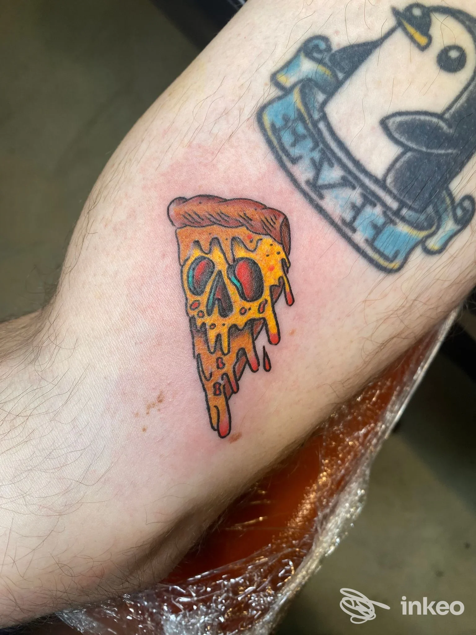 Tatuaggio colorato a forma di fetta di pizza sull'avambraccio, lavoro fotografato presso Tattooing Demon Studio, Roma.