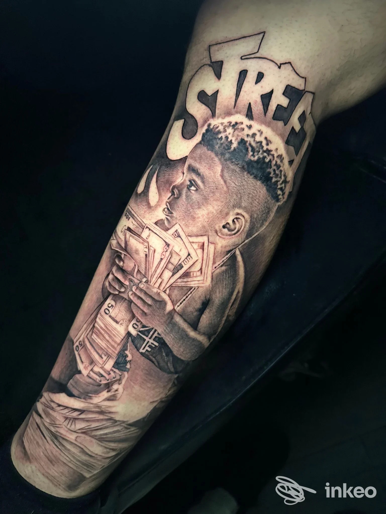 Tatuaggio realistico in bianco e nero su avambraccio raffigurante un bambino con banconote e la scritta STREET, lavoro di Trame Noire, Ladispoli.