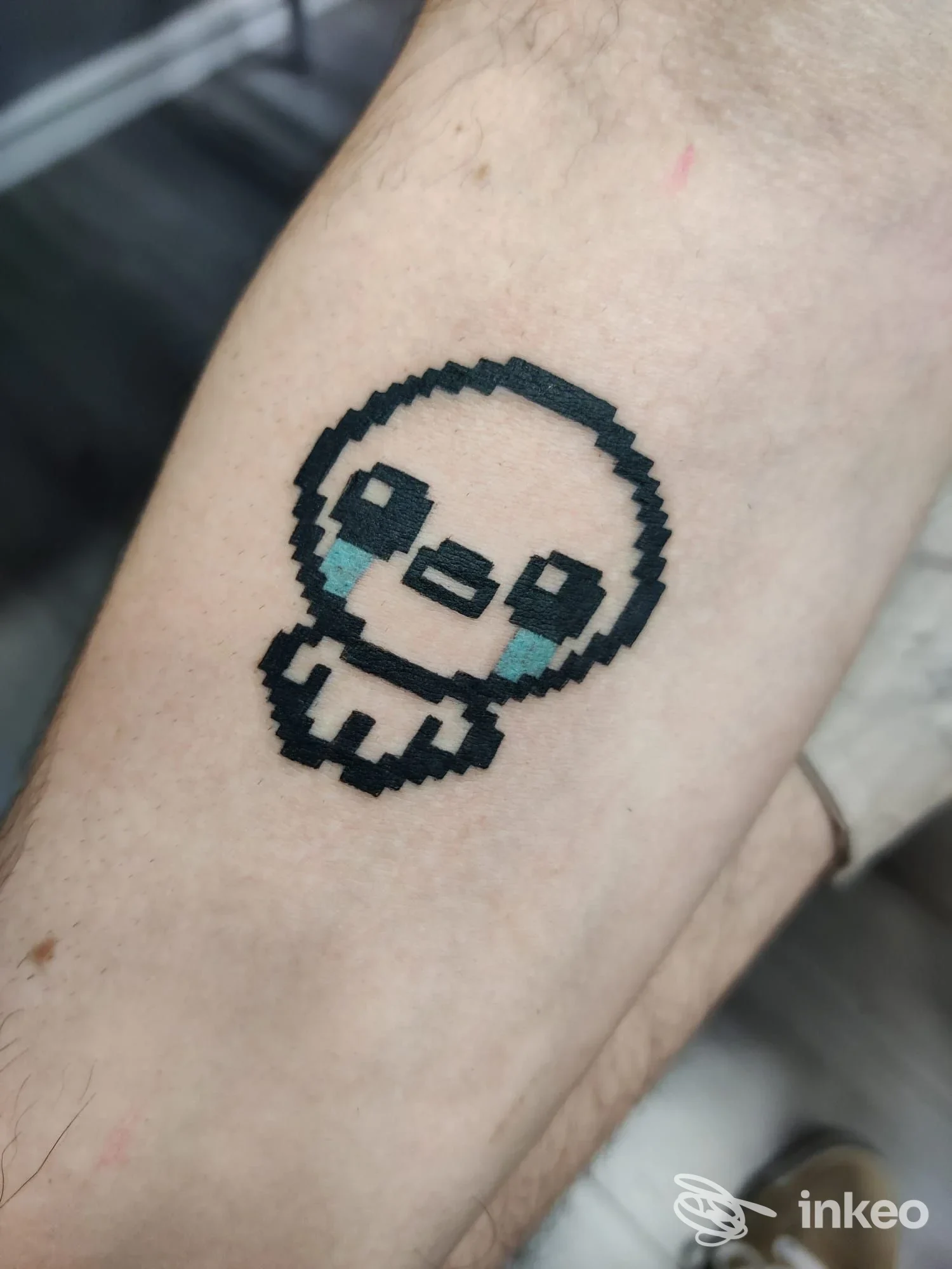 Tatuaggio pixel art su avambraccio: piccolo personaggio stilizzato con occhi e lacrime blu, Vecchie Maniere Tattoo e Piercing, Roma.