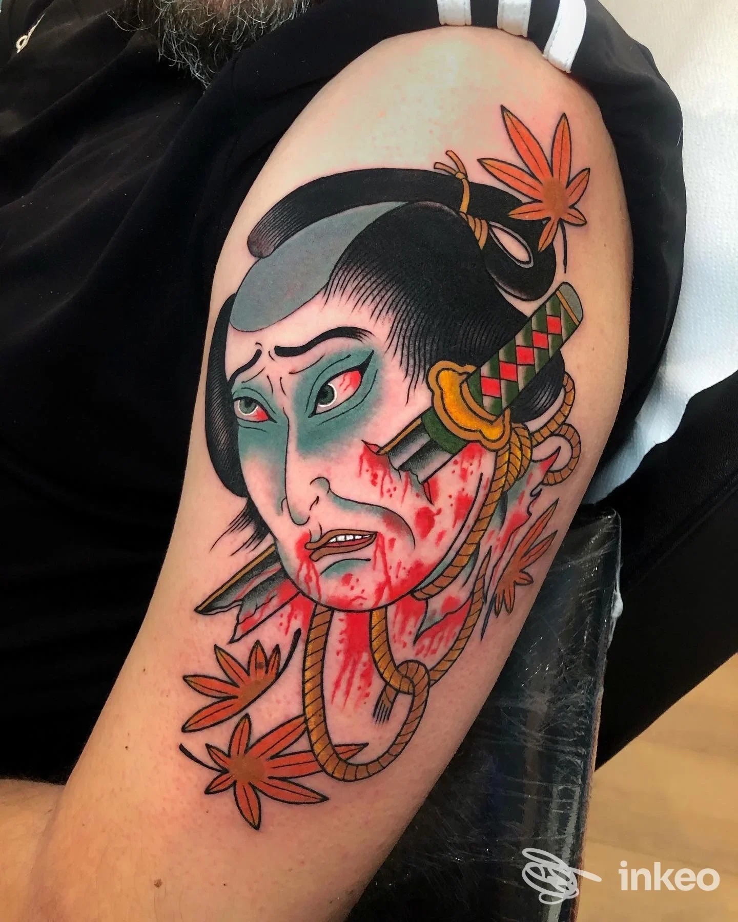 Tatuaggio sul bicipite: volto tradizionale con katana, corde e foglie; foto del lavoro presso Well Done Tattoo Shop, Roma.
