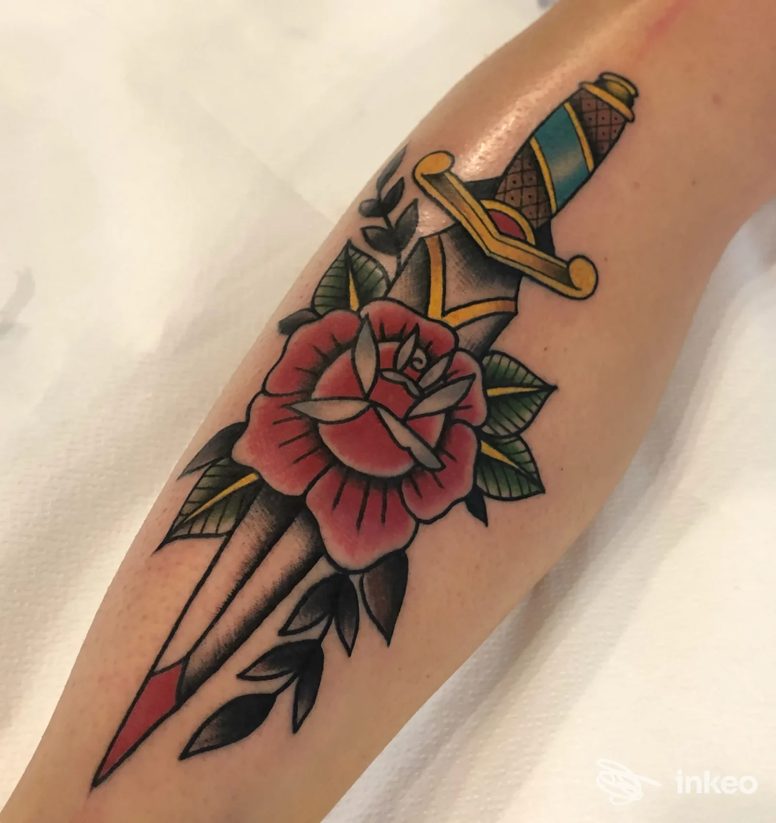 Tatuaggio su avambraccio con pugnale e rosa, scatto dello studio AME Tattoo a Genova che mostra dettagli e colori vividi.