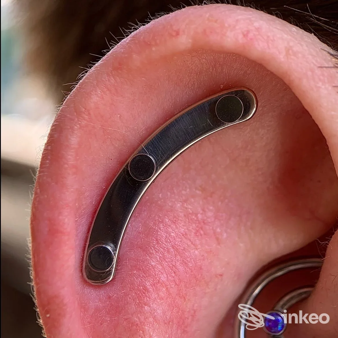 Primo piano di un piercing curvo nella cartilagine dell'orecchio, foto inviata dallo studio ATYPICAL Body Piercing Studio a Genova.