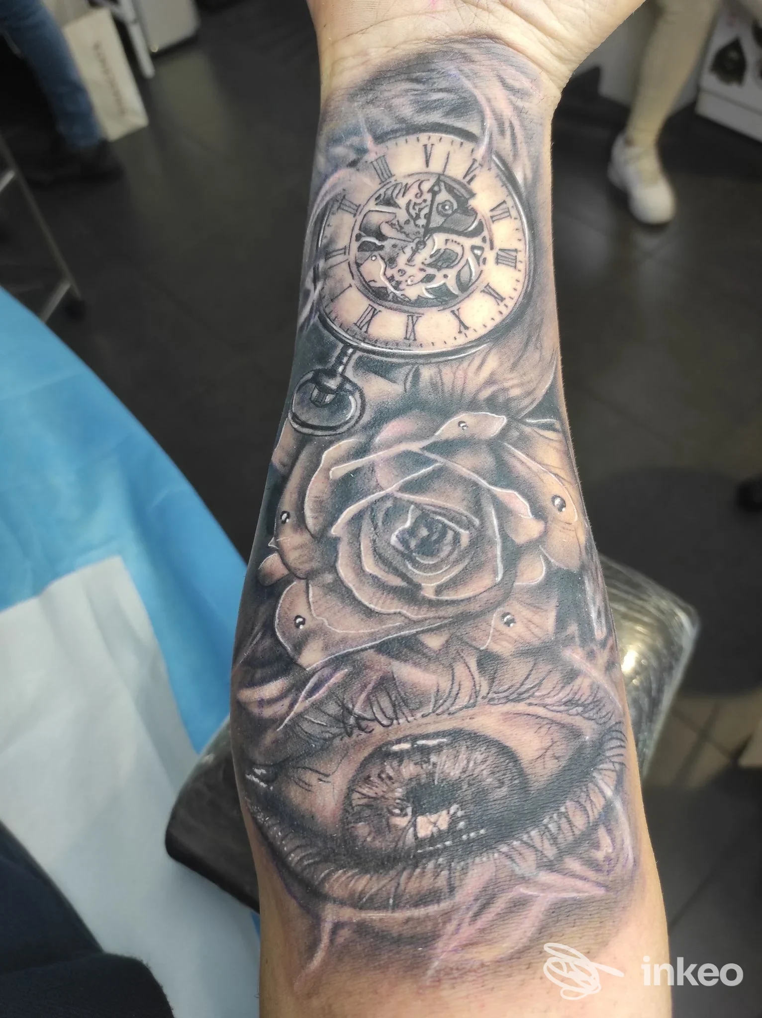 Tatuaggio realistico su avambraccio con orologio da tasca, rosa e occhio, foto dallo studio Ancient Soul Tattoo a Genova.