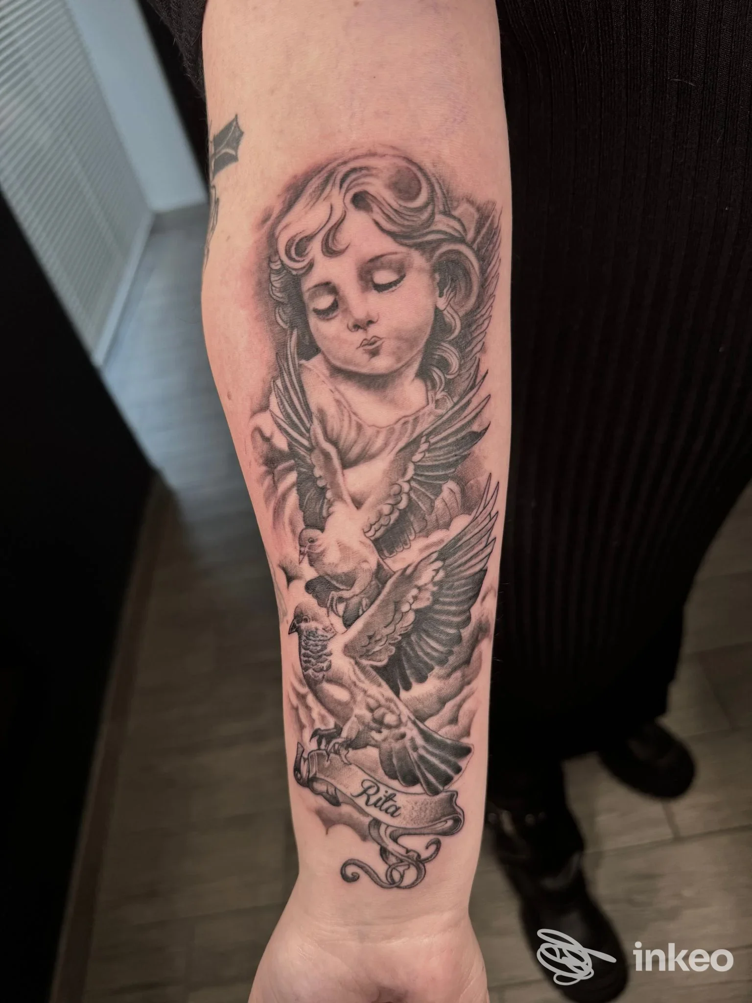 Tatuaggio in bianco e nero su avambraccio con putto e due colombe, lavoro mostrato da Niko Tattoo Studio a Ventimiglia.