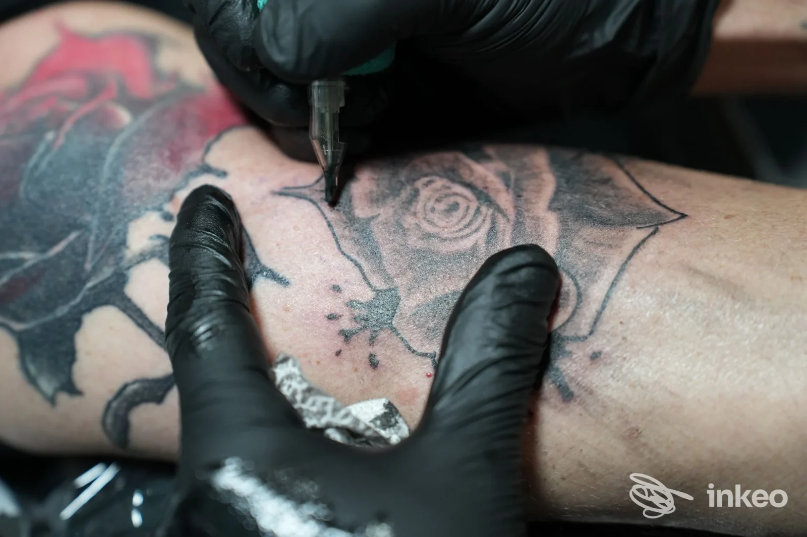 Dettaglio di un tatuaggio a rosa in corso sull'avambraccio, mani con guanti neri e macchinetta — Be happink tattoo, Cairo Montenotte.