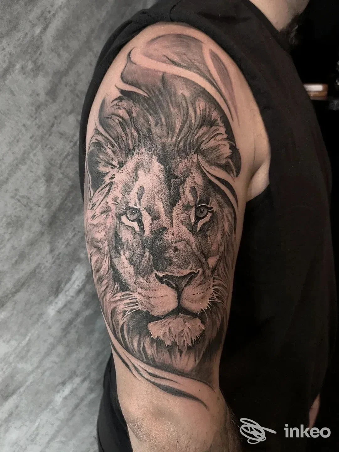 Primo piano di un tatuaggio realistico di leone in nero e grigio sull'omero, realizzato da Black Nun Tattoo, Diano Marina.
