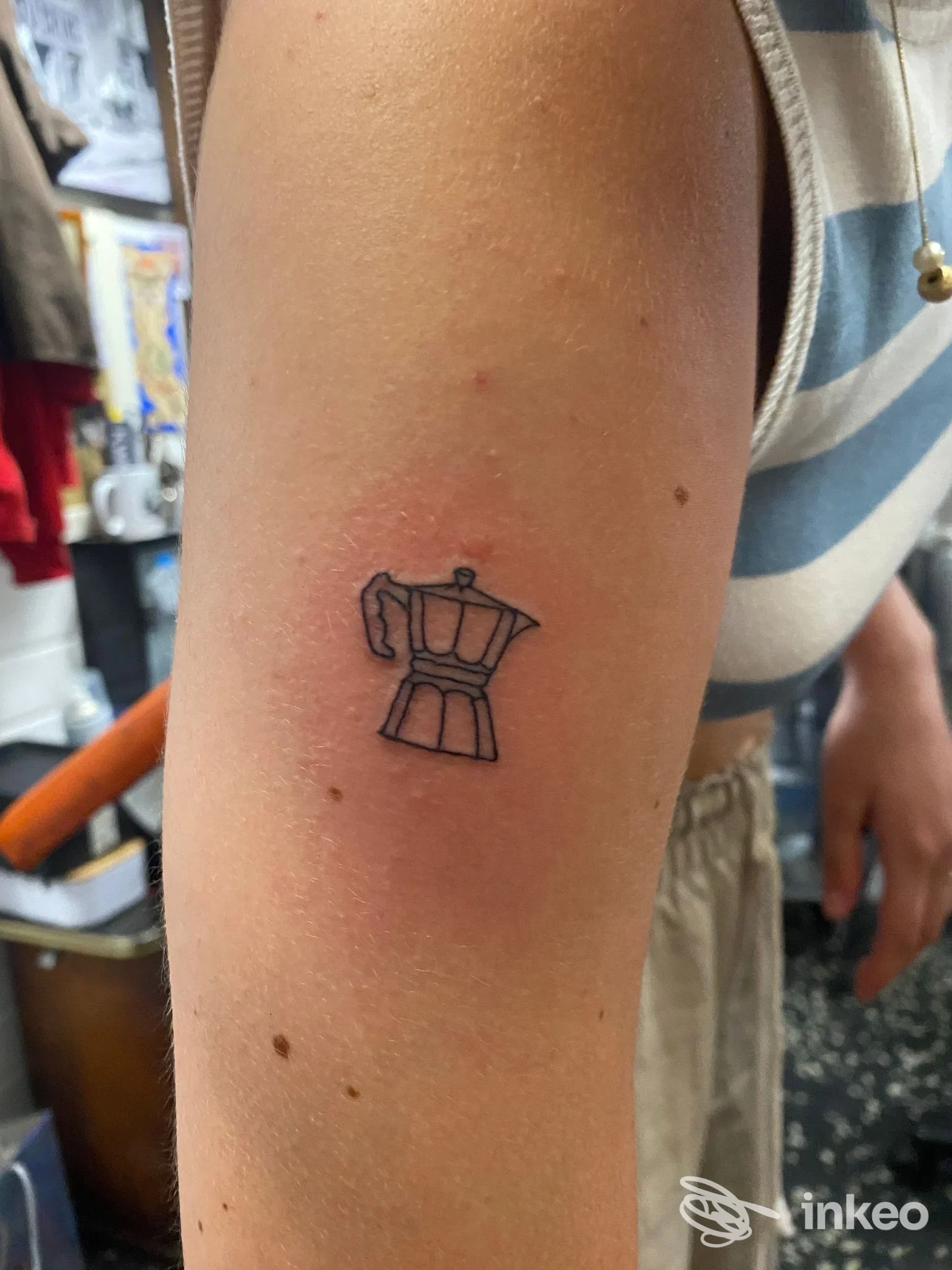Piccolo tatuaggio a linee di una caffettiera sul braccio esterno, eseguito da Blue Port Tattoo a Genova.