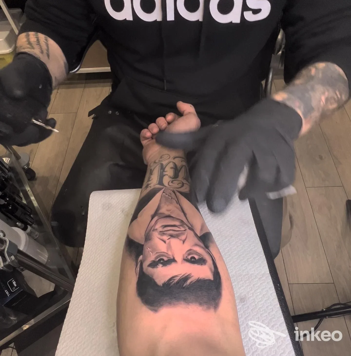 Un avambraccio con tatuaggio realistico raffigurante una testa femminile, eseguito in uno studio di tatuaggi; una persona con guanti lavora sull'avambraccio.
