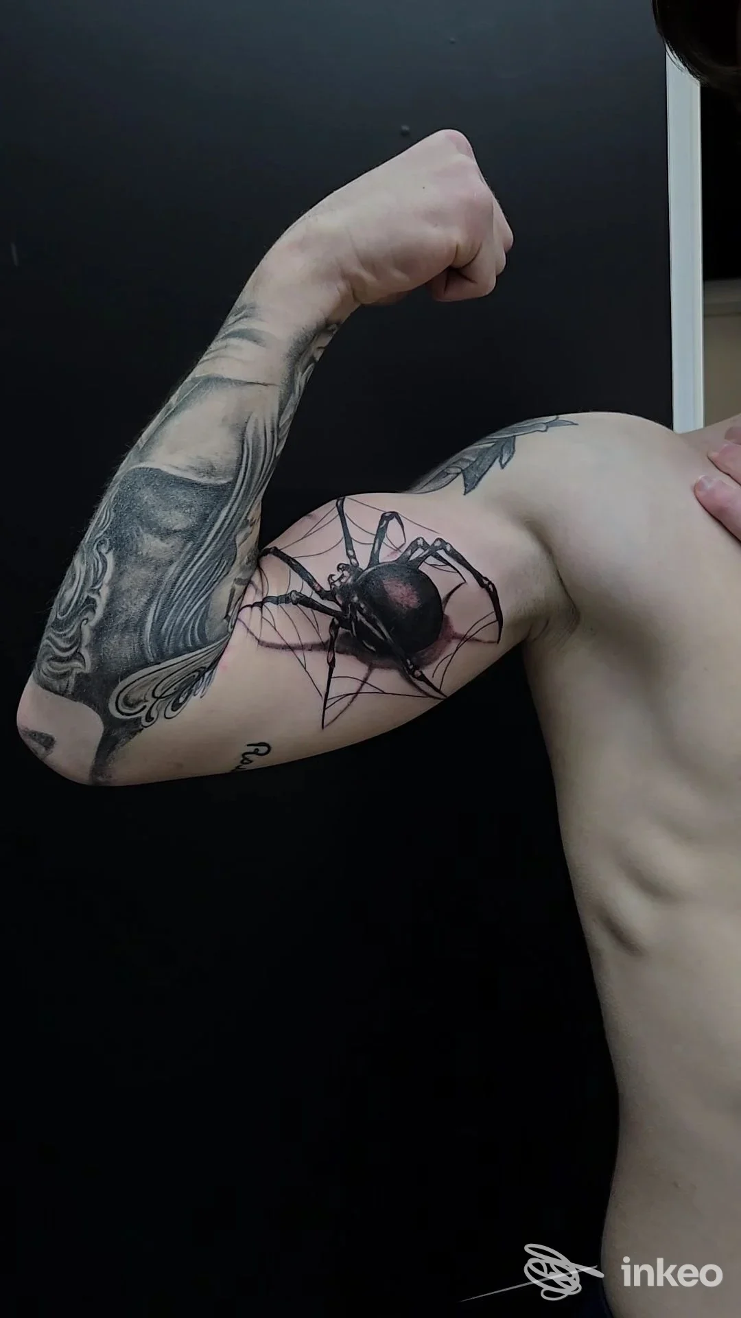 Primo piano di un braccio muscoloso con tatuaggio di ragno sulla pelle, sfondo scuro, senza viso visibile.