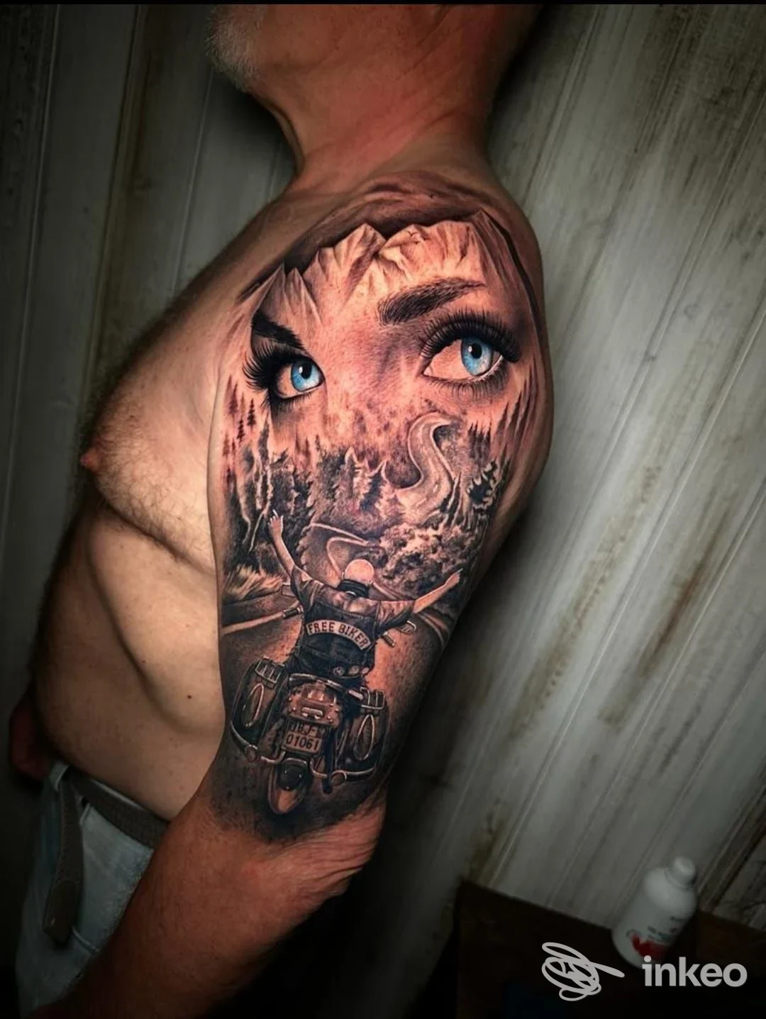 Ampio tatuaggio realistico sulla spalla/braccio con occhi blu, paesaggio montano e motociclista — Civico 47 Tattoo Studio, Albenga.