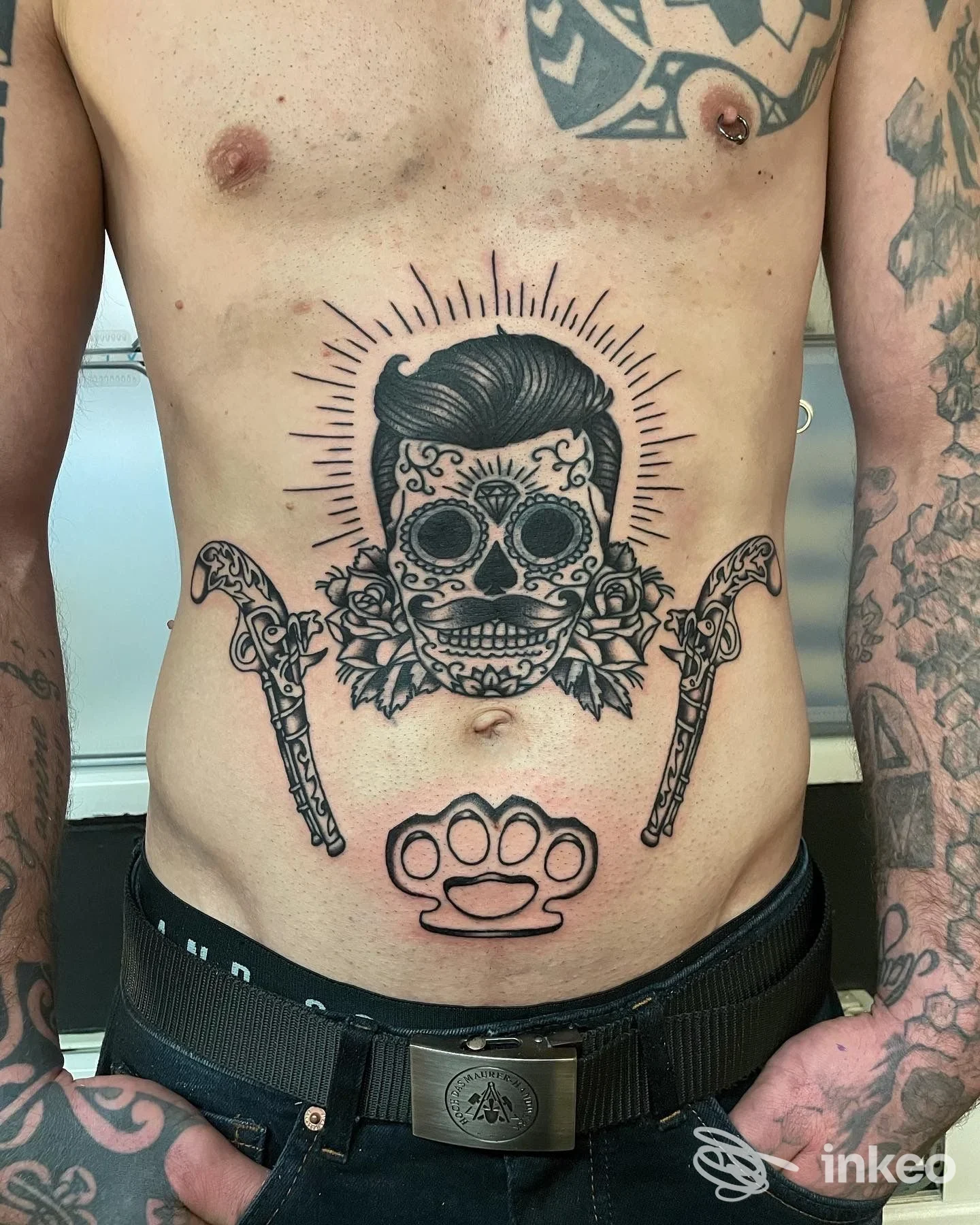 Tatuaggi sul torso: teschio decorativo centrale sull'addome, coltelli laterali e tirapugni sotto. Ettore Groccia Tattoo, Genova.