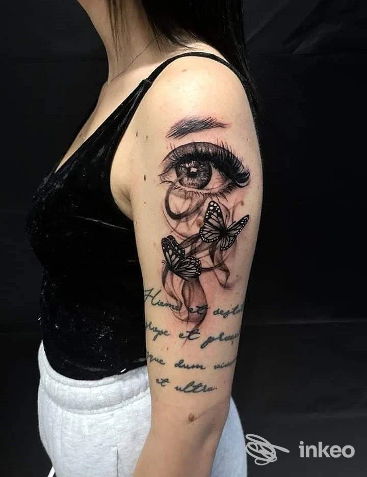 Tatuaggio realistico di occhio con ciglia e farfalle sull'omero, realizzato da Eudemonìa Tattoo Atelier a Sarzana.
