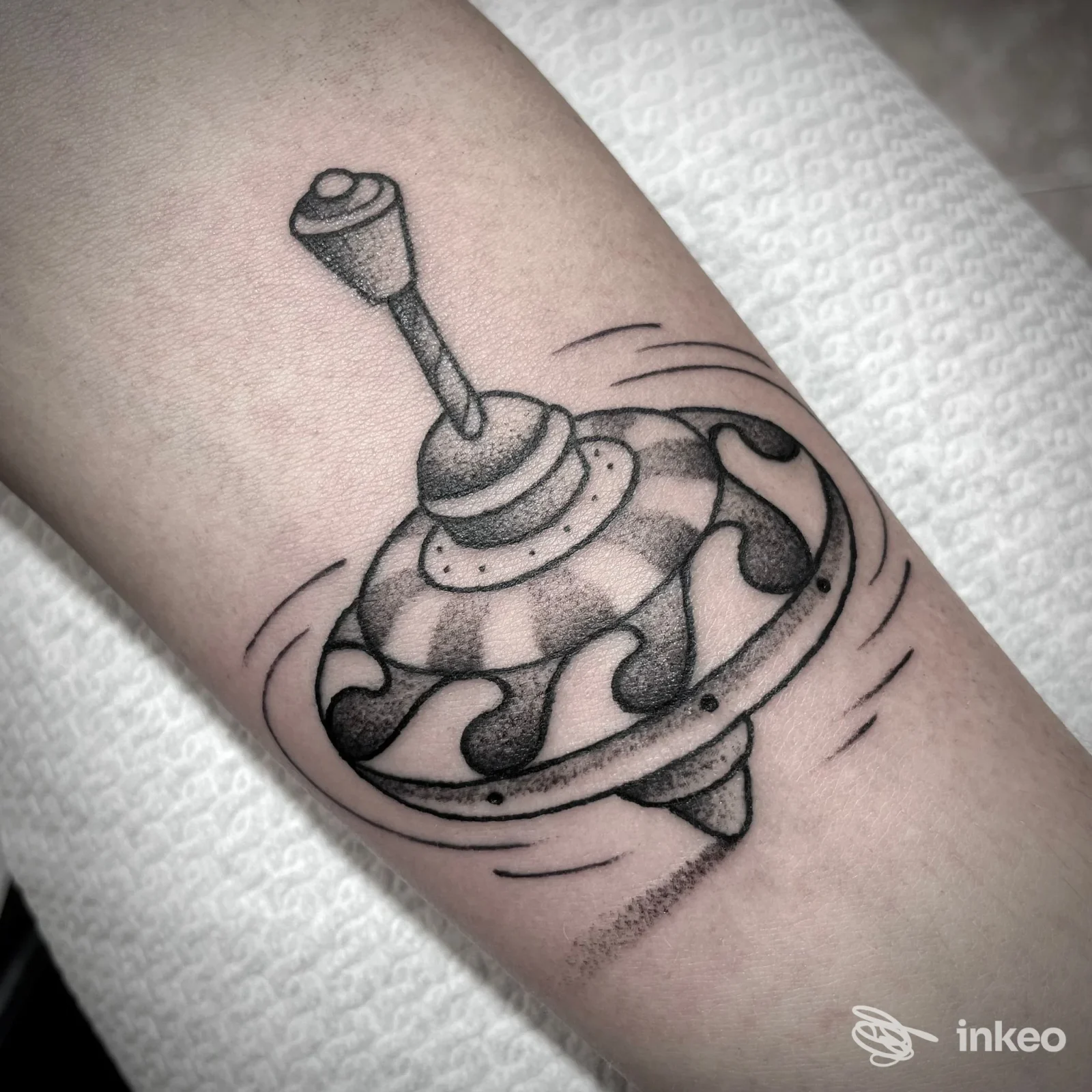 Tatuaggio in bianco e nero raffigurante una trottola in movimento sull'avambraccio, realizzato al Goa Tattoo Shop di Genova.
