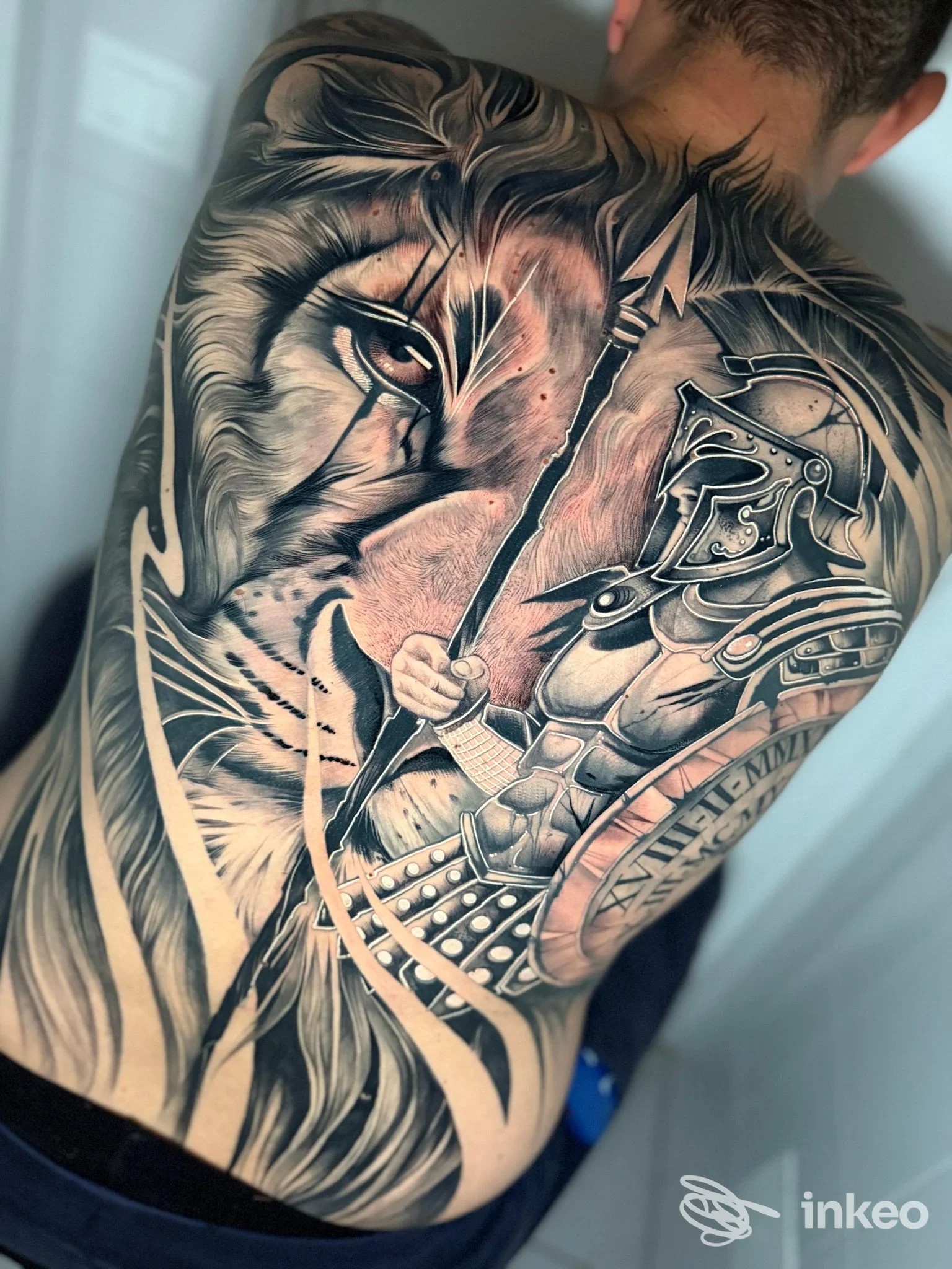 Grande tatuaggio realistico a tutta schiena con leone e guerriero, fotografato per Good Mornink Tattoo Studio ad Albisola Superiore.