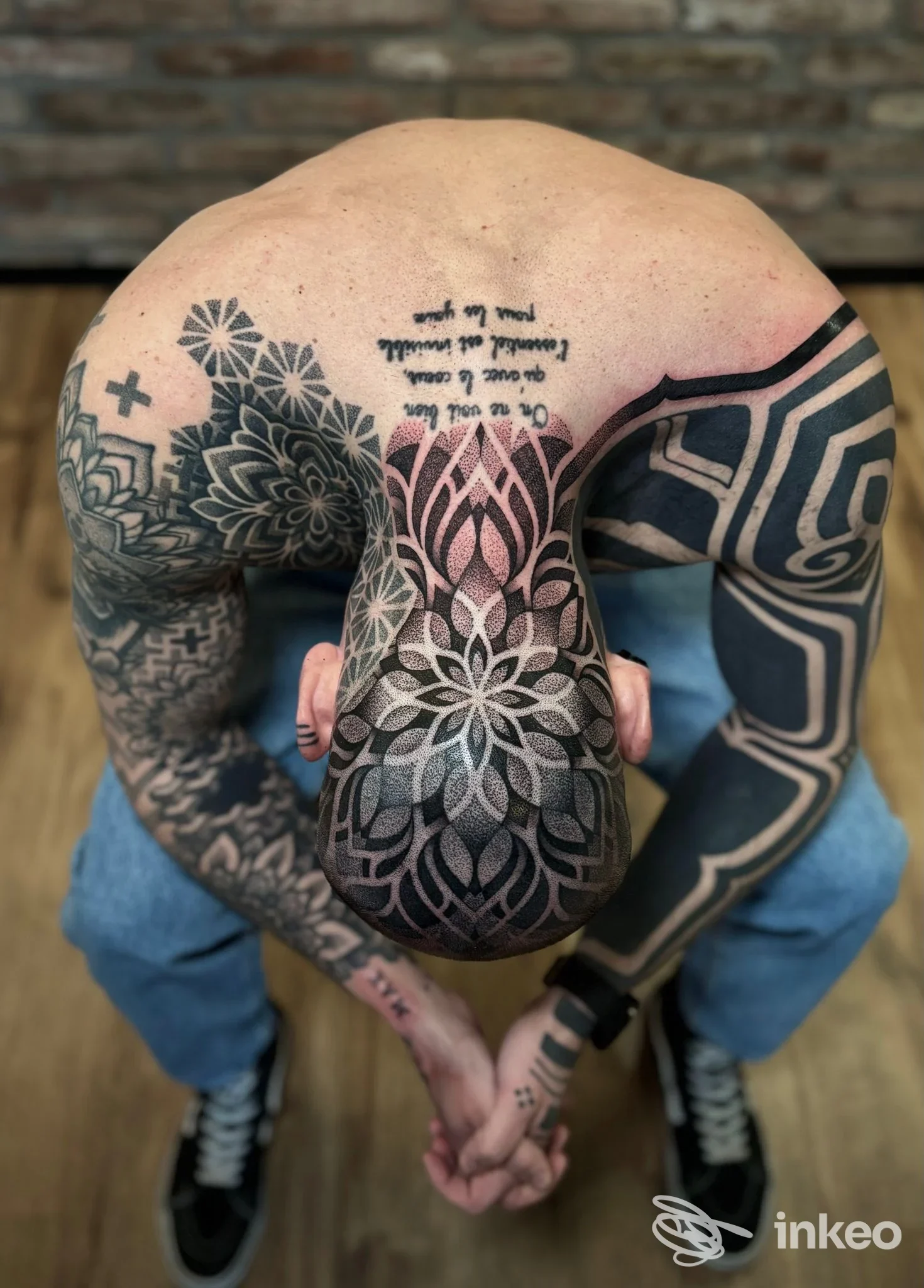 Tattoo grande a coprire schiena e braccia di una persona, stile geometrico e floreale in tonalità scure, scatto dall'alto con la testa inclinata.