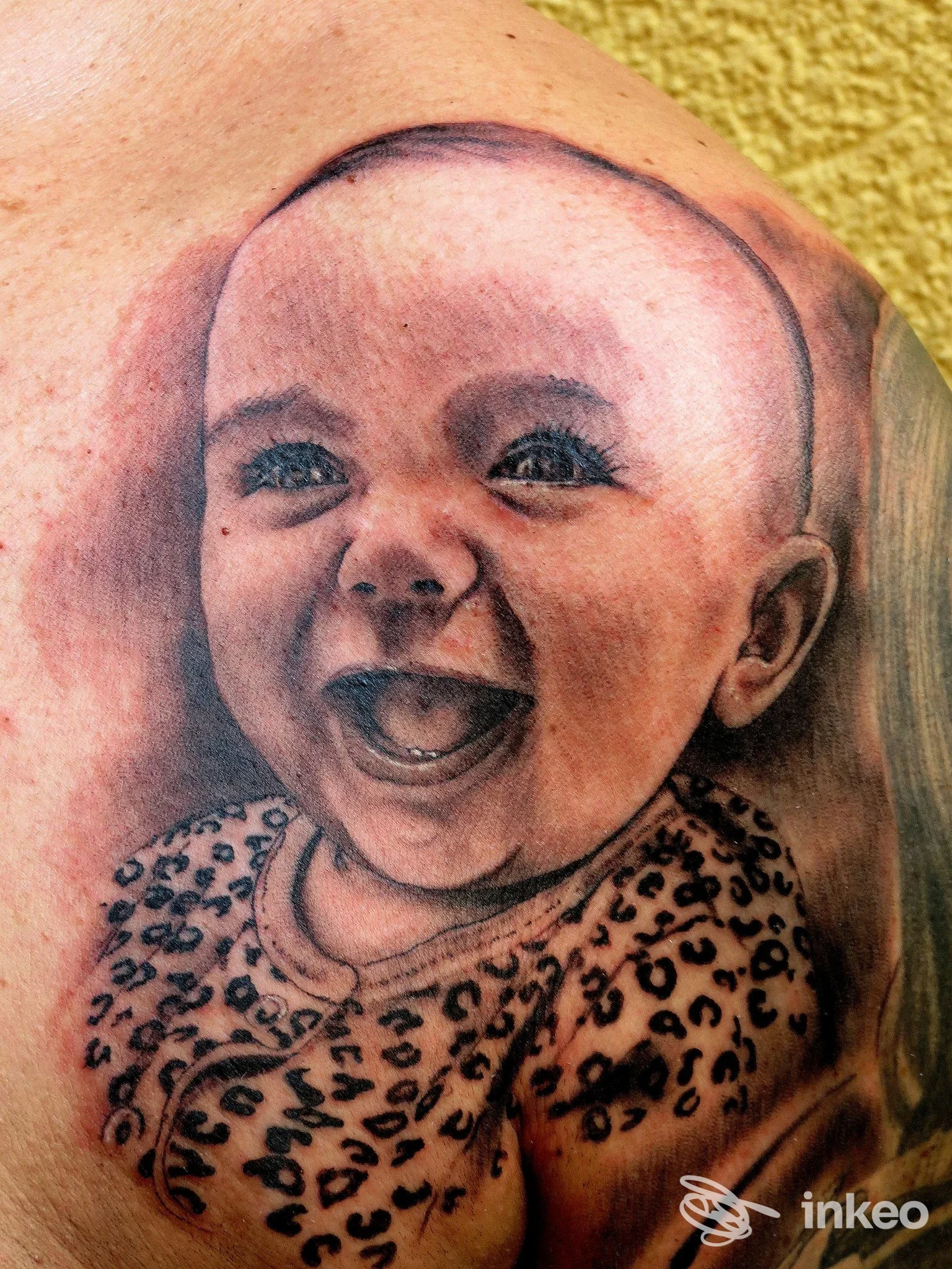 Tatuaggio ritratto realistico di un neonato sorridente sulla spalla, dettaglio del volto e del body maculato, Igor Tattoo, Sanremo.