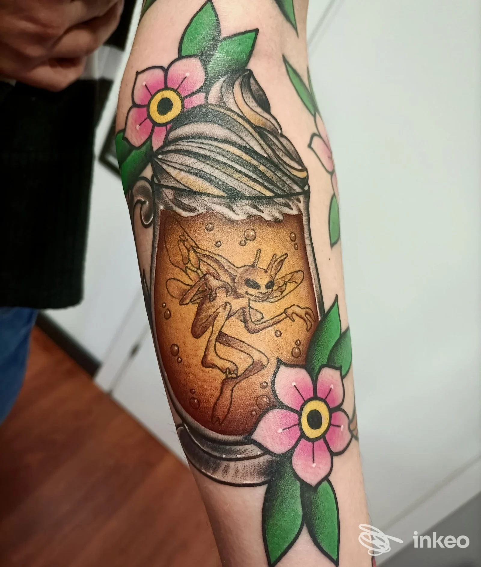 Tatuaggio su avambraccio raffigurante un boccale con una creatura in liquido e fiori, LAVAGNA TATTOO SHOP, Lavagna.