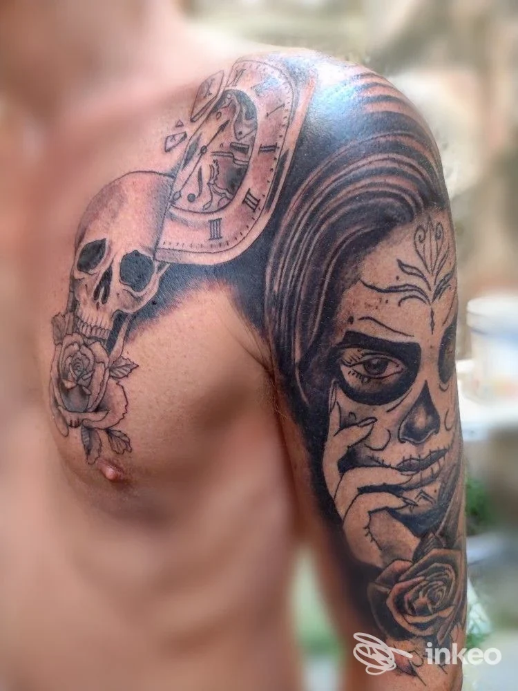 Tatuaggio black & grey su spalla, alto braccio e pettorale con teschio, orologio e volto femminile — Inkplosion Tattoo, Genova.