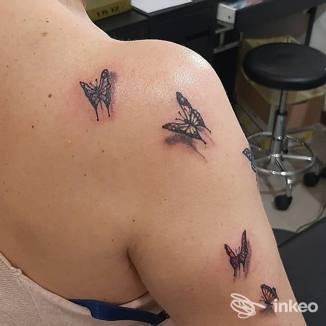 Dettaglio di piccoli tatuaggi a forma di farfalla sulla spalla e il braccio superiore, scattato presso La stella nera Tattoo a Genova.