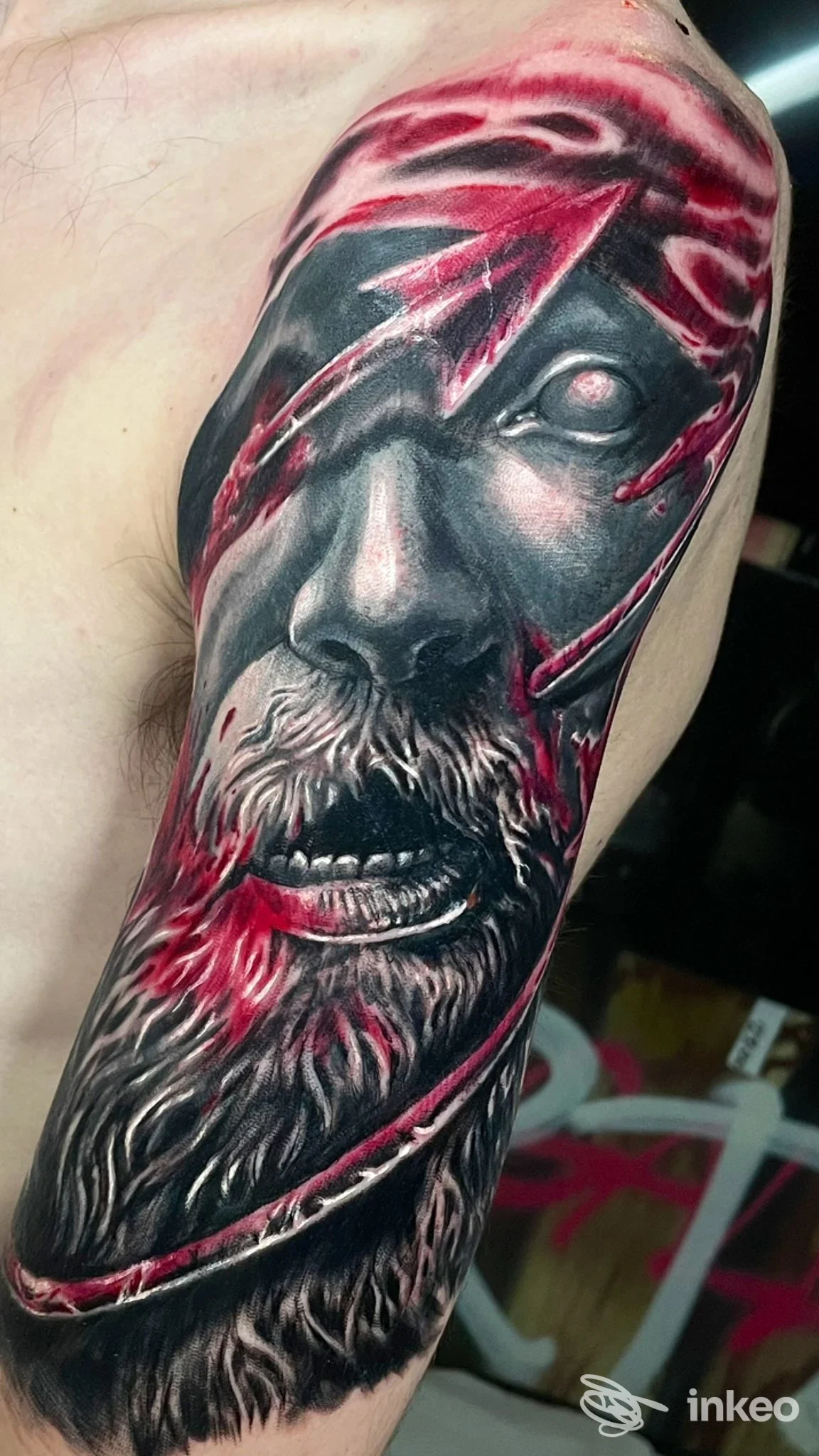 Tatuaggio realistico su spalla e bicipite con volto strappato in nero/grigio e accenti rossi — La Grande Bellezza Tattoo Gallery, Genova.