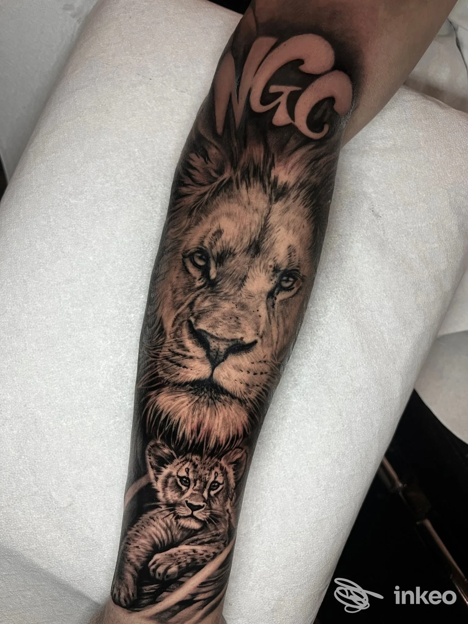 Avambraccio con tatuaggio realistico in nero/grigio raffigurante un leone e un cucciolo. Mara Tattoo Shop, Bottagna.