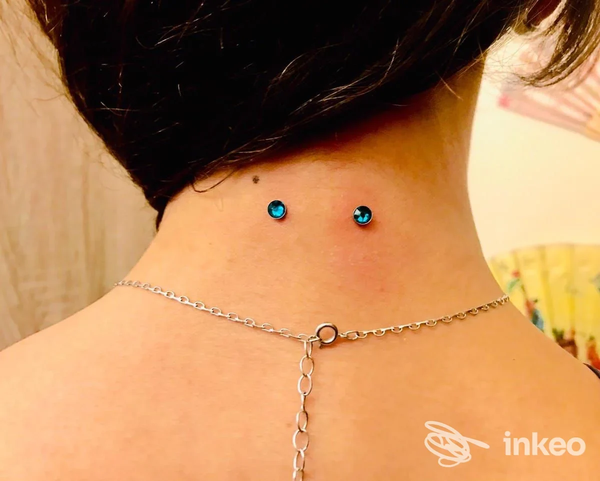 Due microdermal con gemme azzurre sulla nuca, piercing fotografato dal retro; immagine correlata a Moai Body Piercing, Genova.