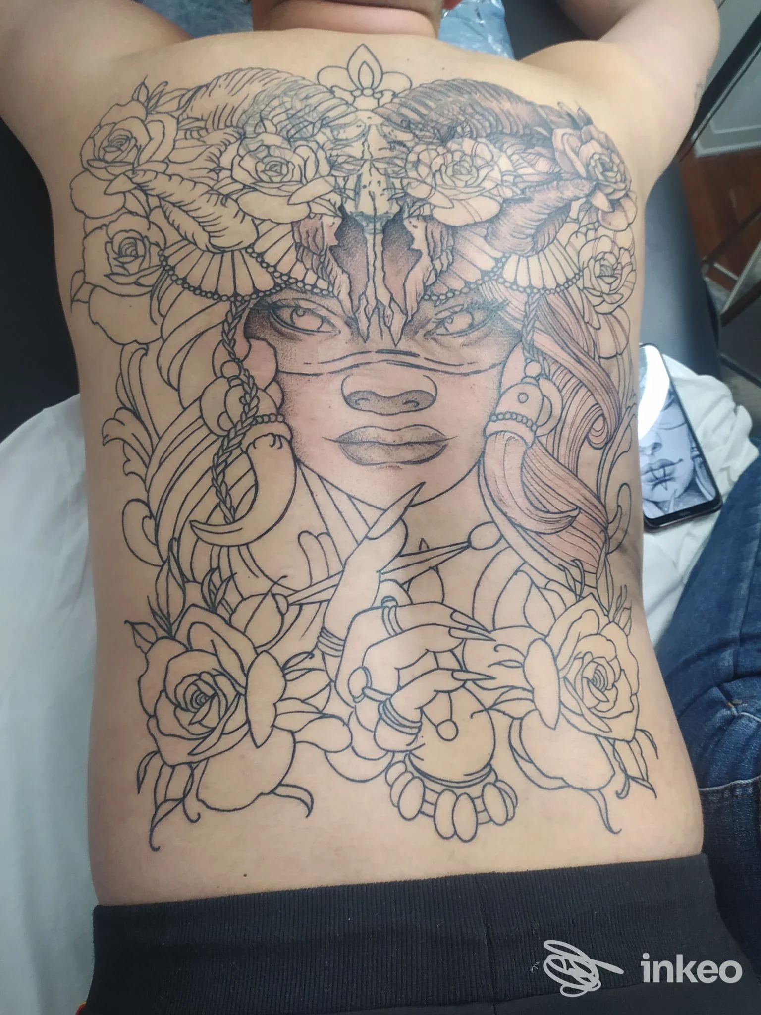 Grande tatuaggio a linee nere che copre tutta la schiena con volto stilizzato e decorazioni floreali, fotografato presso Moonflower Tattoo Studio ad Albenga.