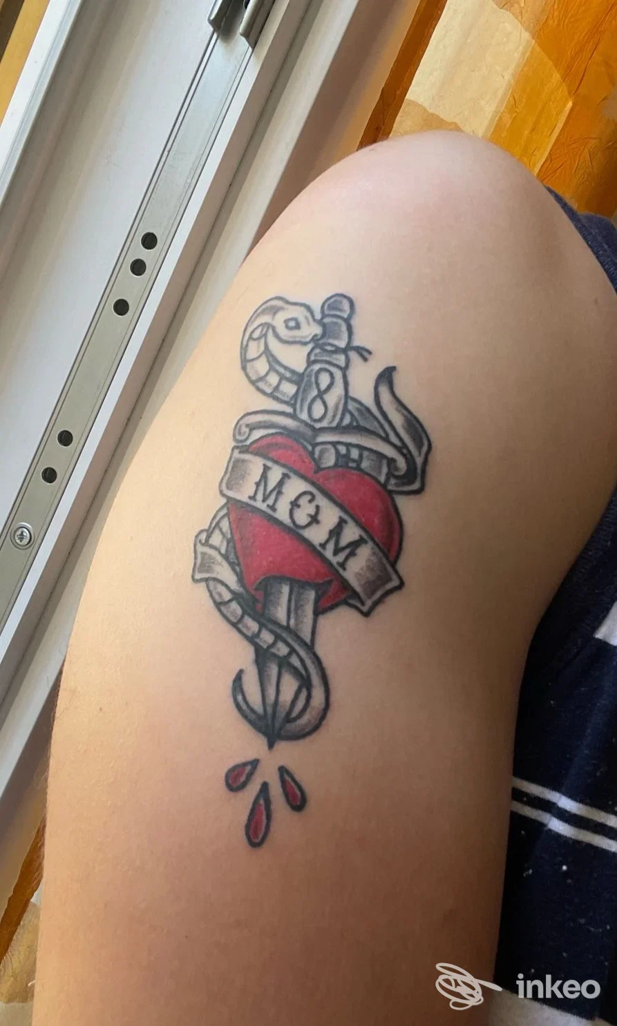 Tatuaggio tradizionale a cuore e pugnale con nastro "M&M" sul bicipite, foto di Narciso Tattoo and Fine Art, Imperia.