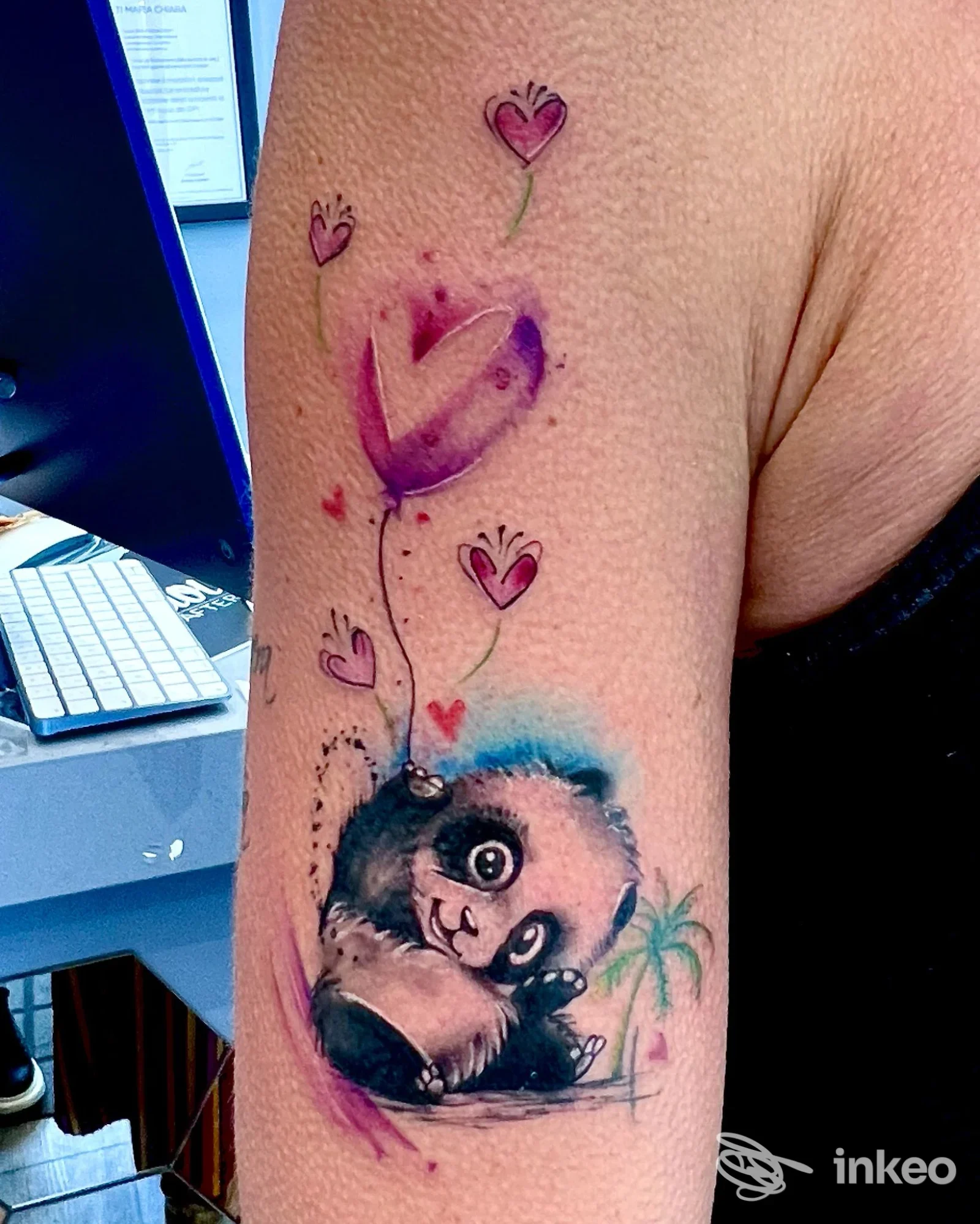 Tatuaggio su parte superiore del braccio con panda colorato e cuori, foto fornita da Next Tattoo, Genova.
