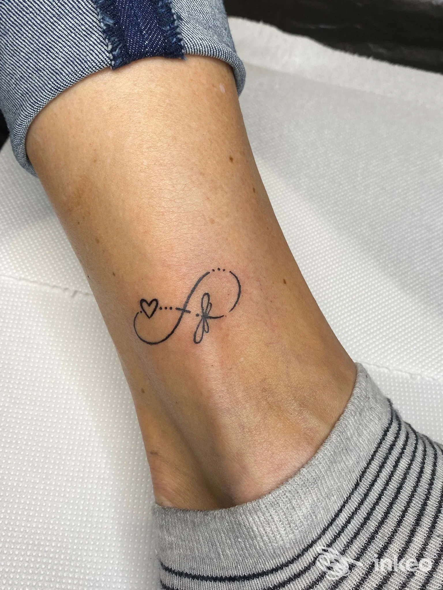 Tatuaggio minimal alla caviglia con cuore e motivo a infinito eseguito da Old Town Tattoo Shop, Chiavari.