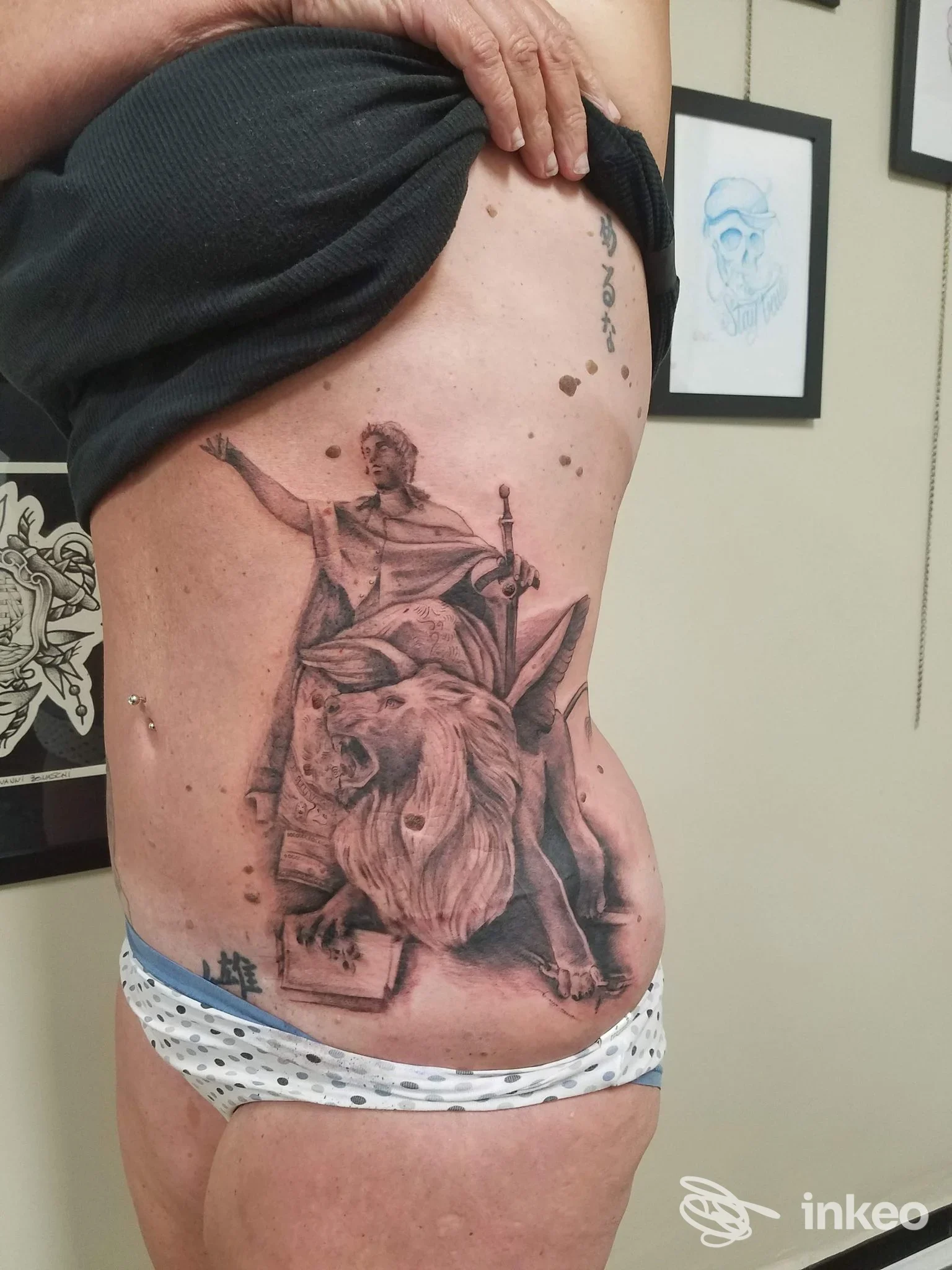 Grande tatuaggio in bianco e nero raffigurante una figura con un leone sul fianco di una persona, Orione Tattoo Imperia.