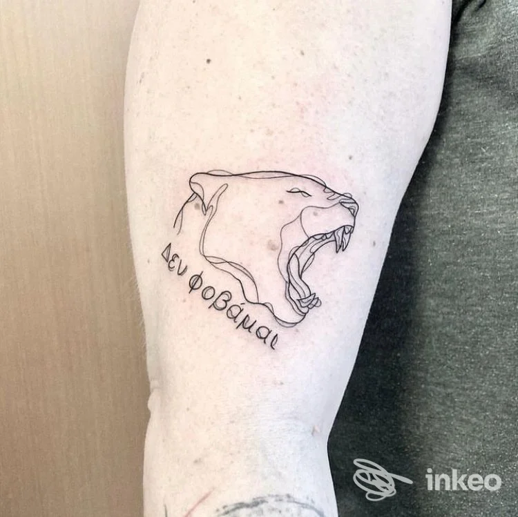 Tattoo visibile sul braccio: profilo di orso in stile outline con la bocca aperta e una scritta curva sotto, realizzata direttamente sulla pelle.