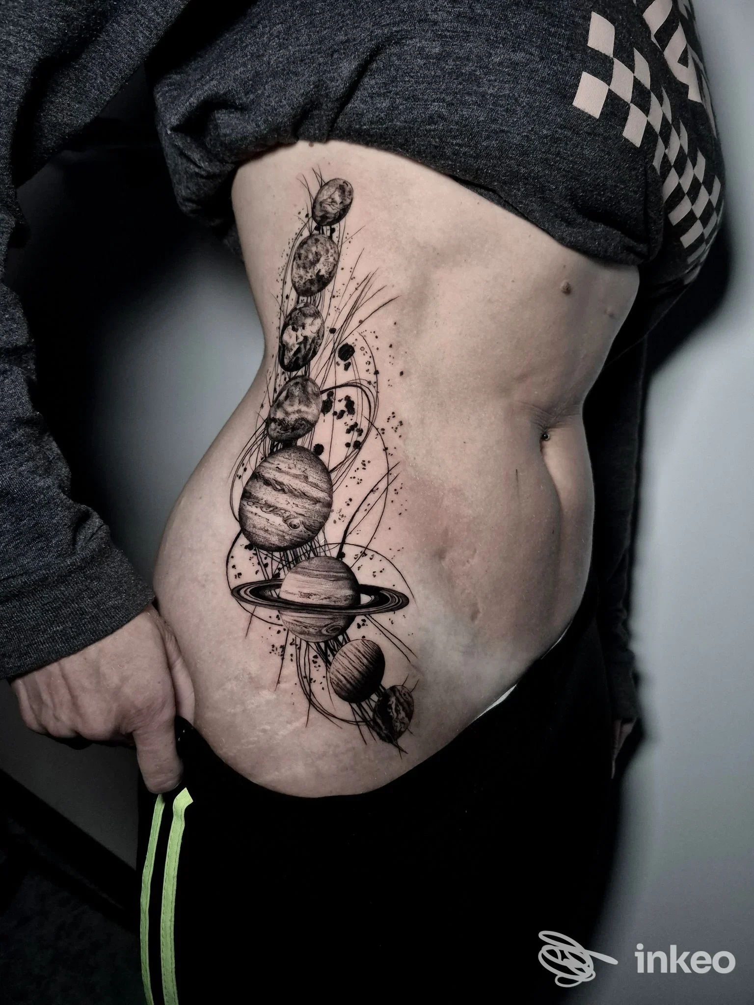Tatuaggio a inchiostro nero con sistema solare a colonna sul fianco; Romeo & Juliet Tattoo Studio, Savona.