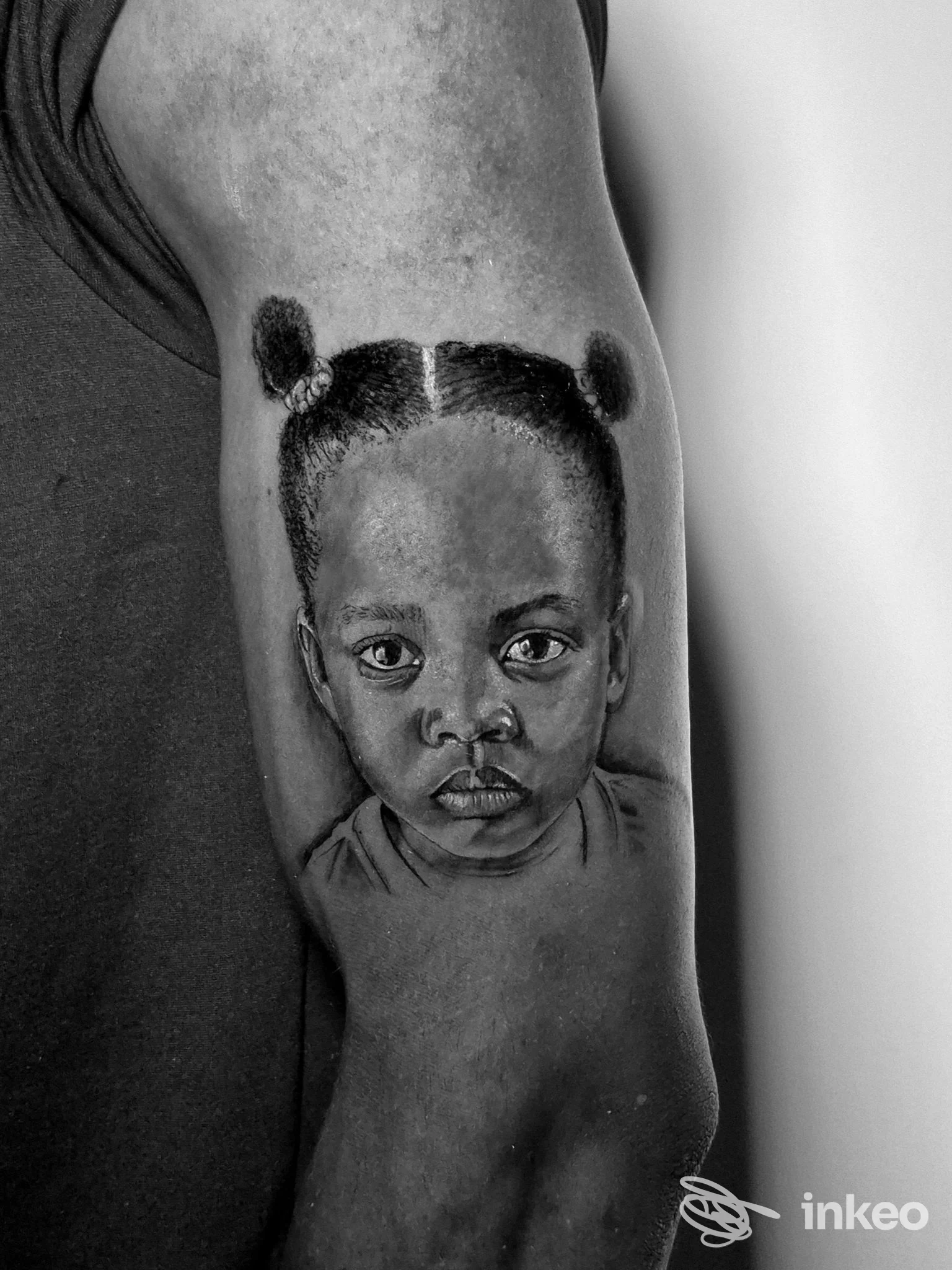 Tatuaggio realistico in bianco e nero di un volto di bambina sull'avambraccio, foto proveniente da Romeo & Juliet Tattoo Studio, Savona.