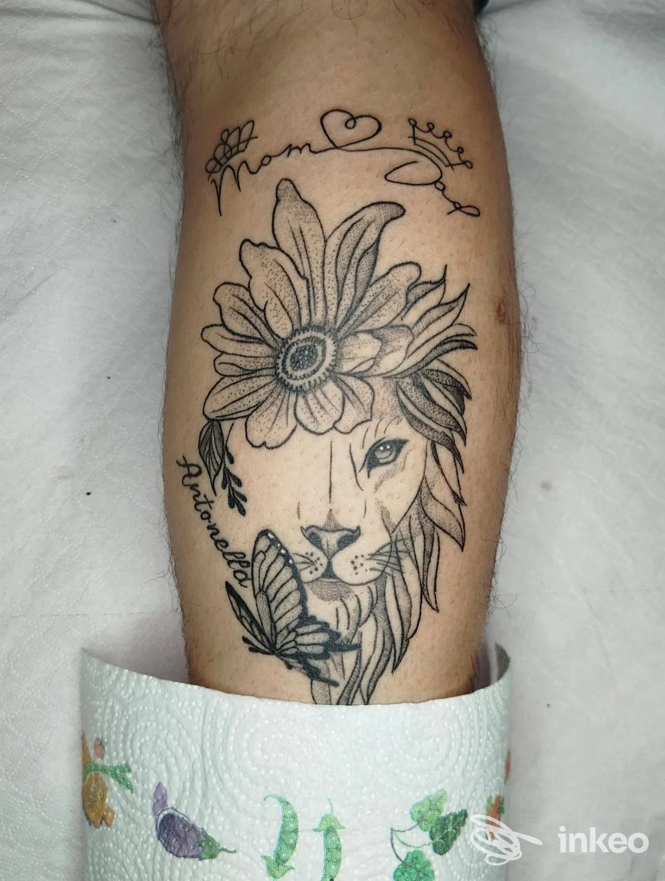 Tatuaggio su polpaccio: mezzo volto di leone con fiore e farfalla, immagine in bianco e nero. Pink Lady Tattoo, Genova.