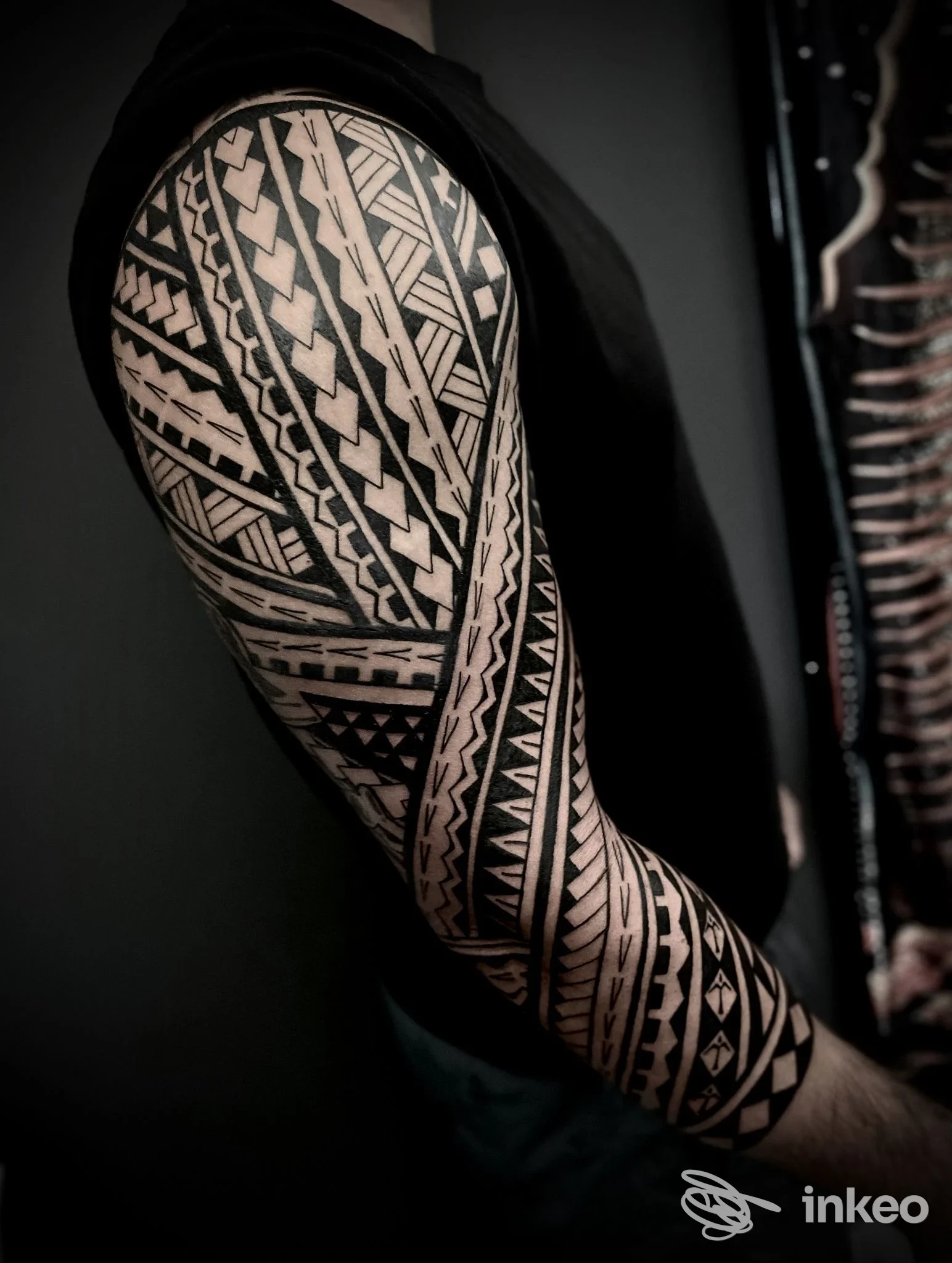 Manica tribale nera su braccio fotografata per Rafa Ferrari Tattoo Studio, Imperia; contrasto elevato su sfondo scuro.
