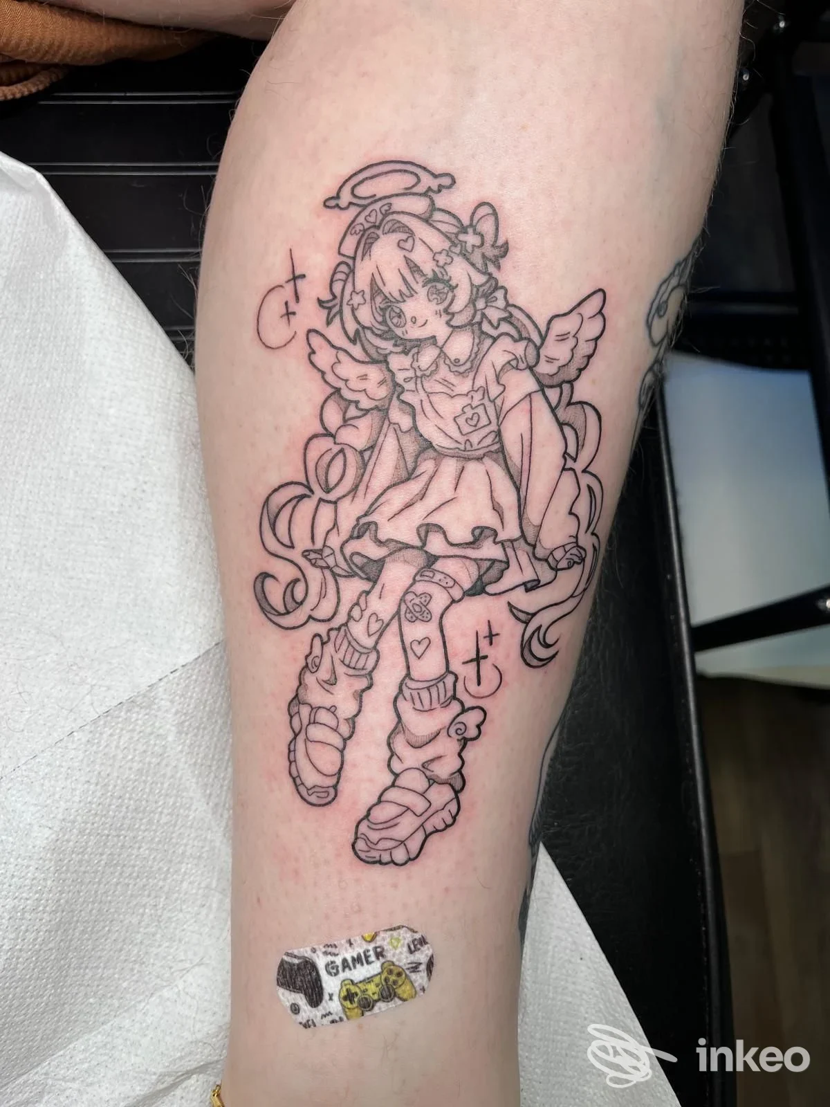 Tattoo su avambraccio raffigurante una ragazza anime con ali, realizzata con linework in nero; una piccola spilletta adesiva si trova sul bordo inferiore della foto.