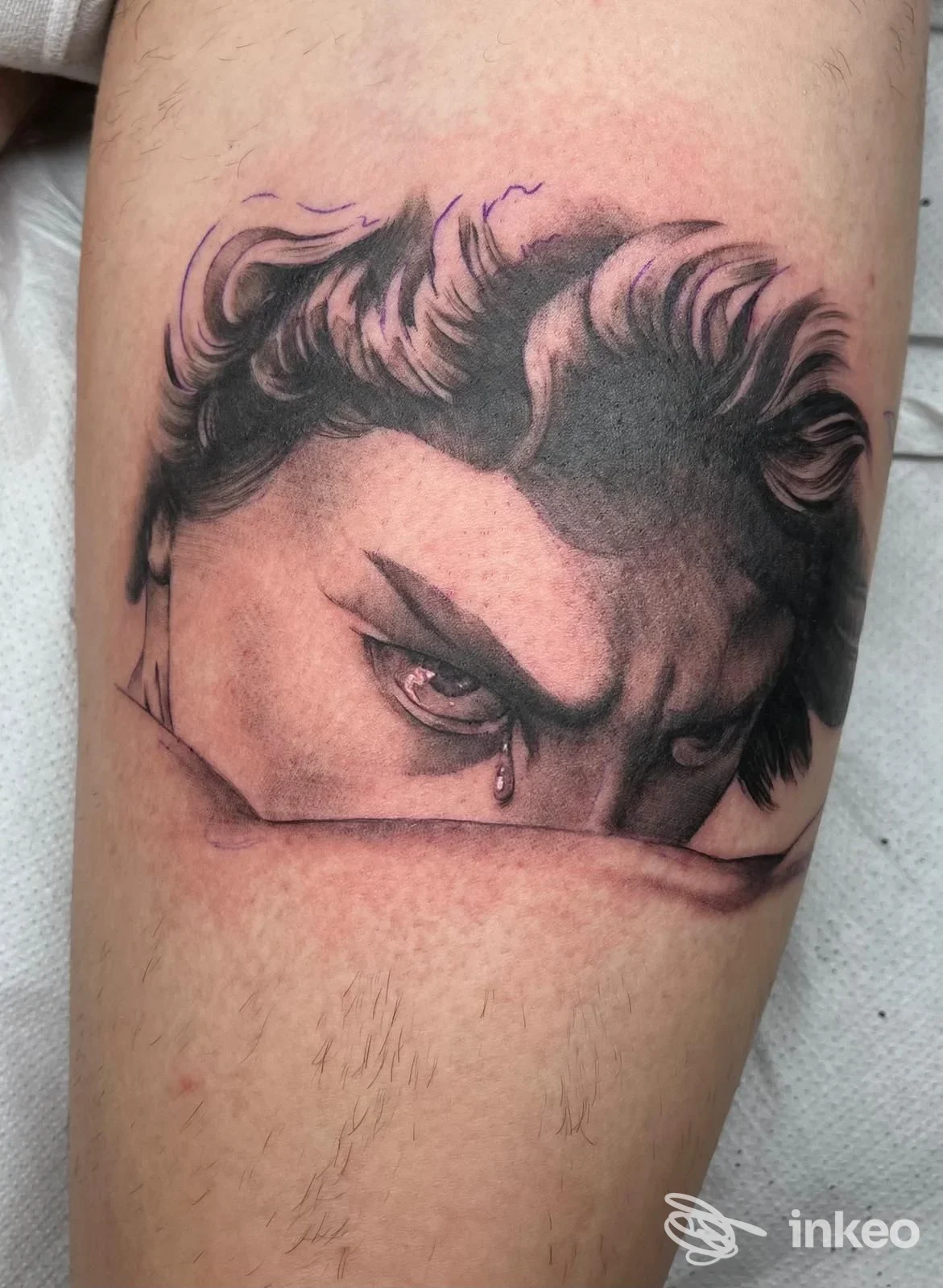 Tattoo su avambraccio raffigurante un volto intenso con occhi fissi; nessun overlay sociale visibile; inquadratura parziale del volto.