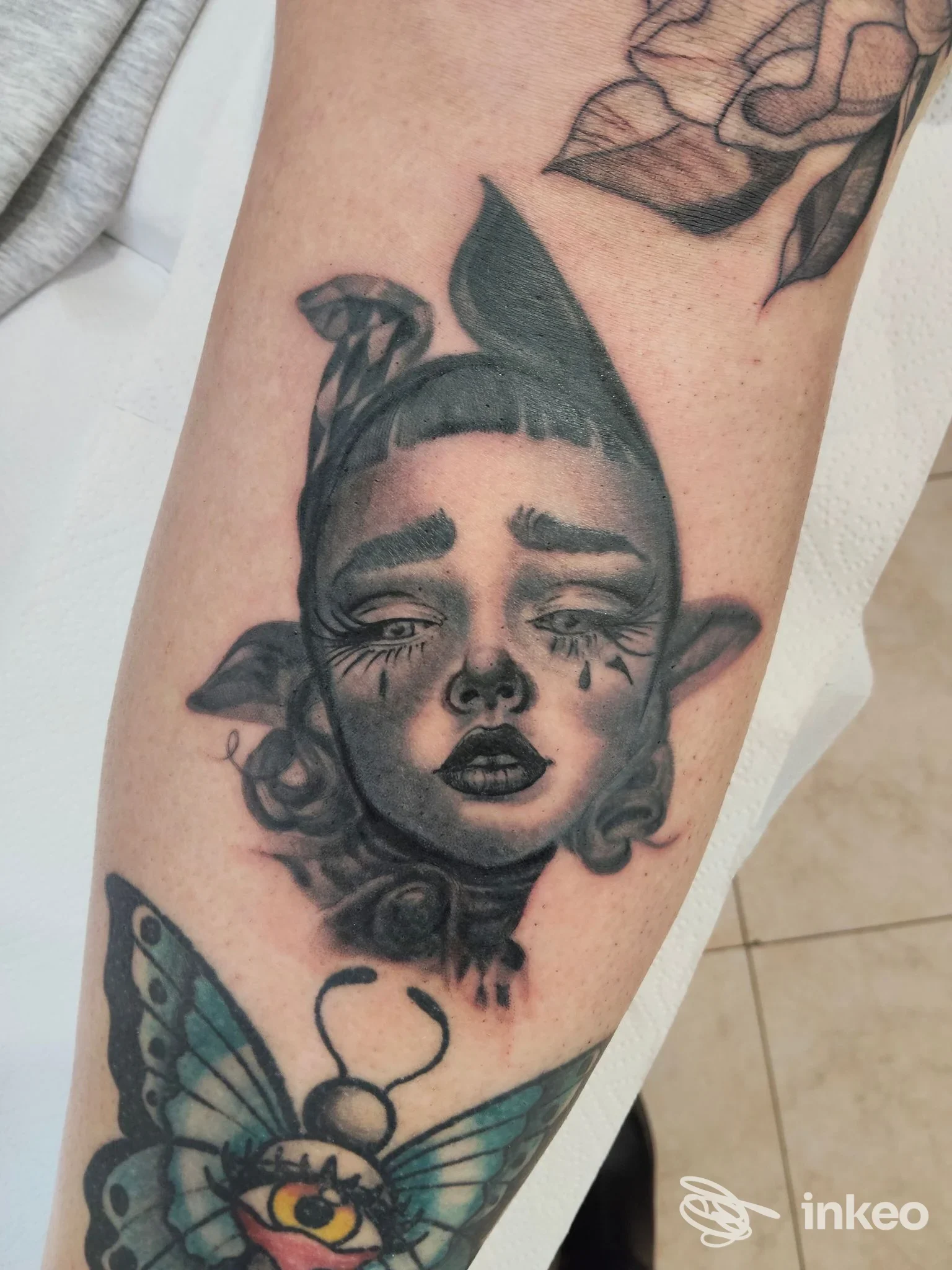Tatuaggio su avambraccio con volto stilizzato in bianco e nero e farfalla colorata, Stranger Skin Tattoo, Genova.